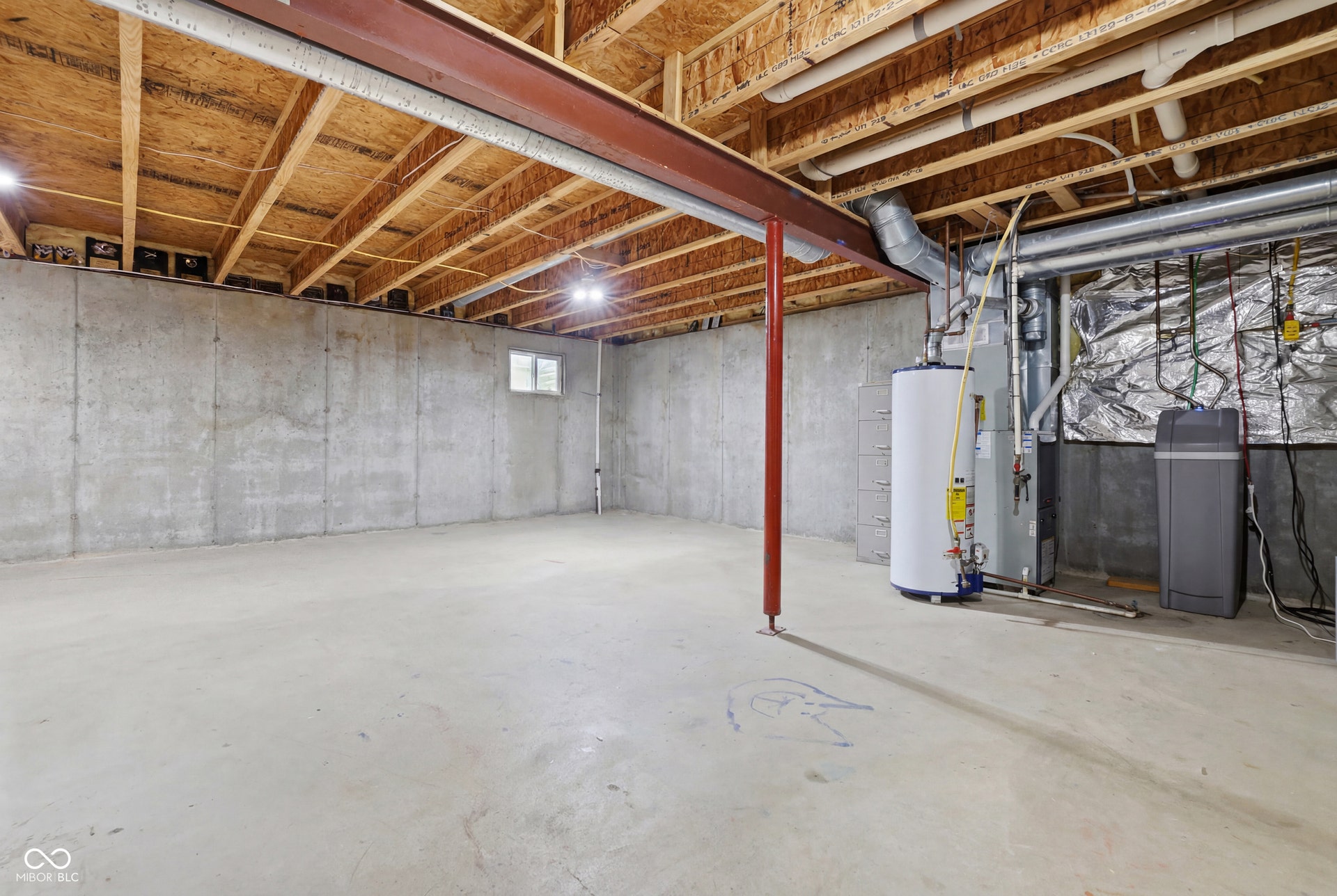 Spacious unfinished basement featuring concrete flooring, exposed wood joists, a small window, water heater, and water softener system