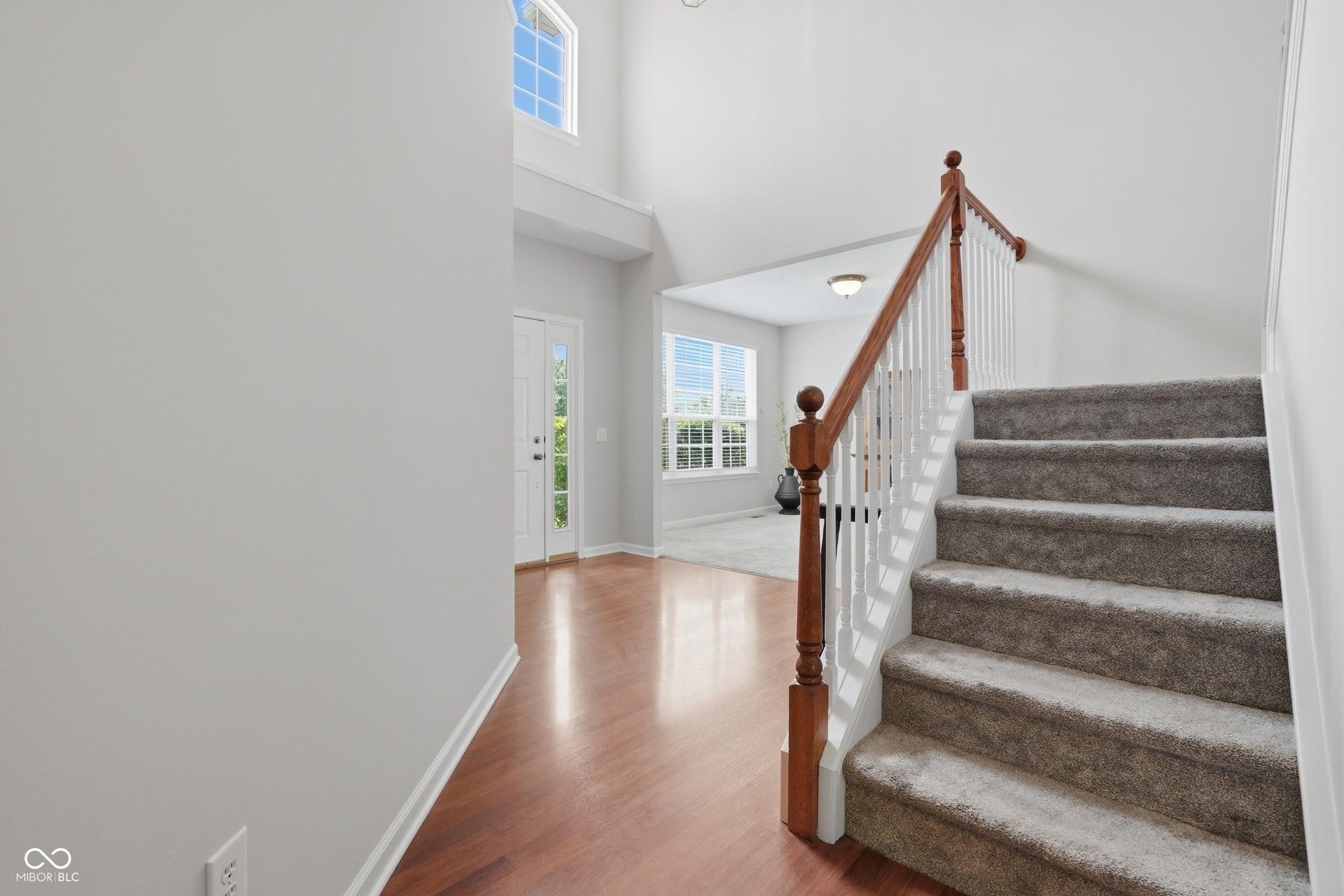 Two-story foyer featuring wood-finish flooring, a carpeted staircase with wood banister and white spindles, and an abundance of natural light