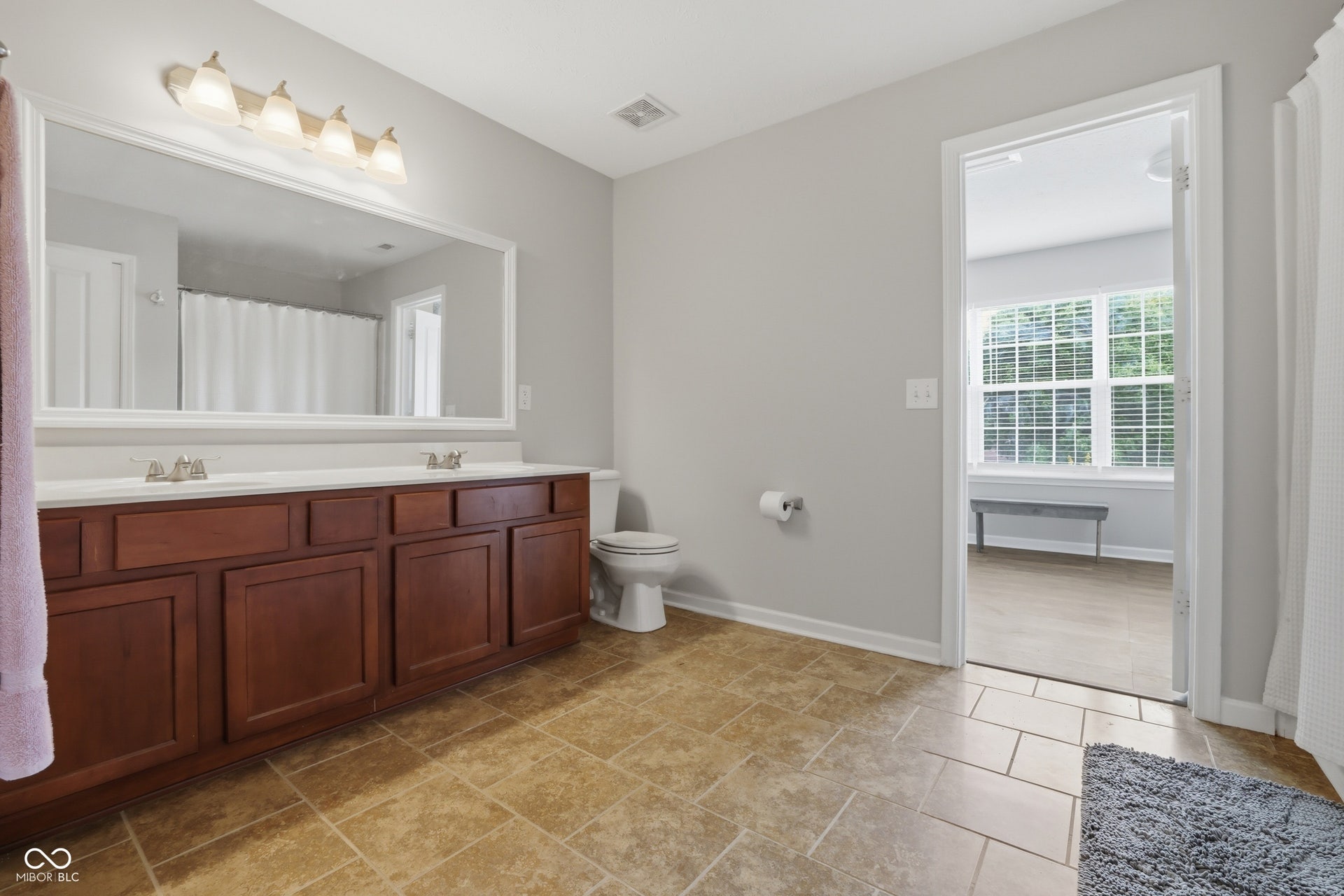 Bathroom featuring a dual vanity with a white countertop and wood-finish cabinetry, a large wall-mounted mirror, and tile flooring