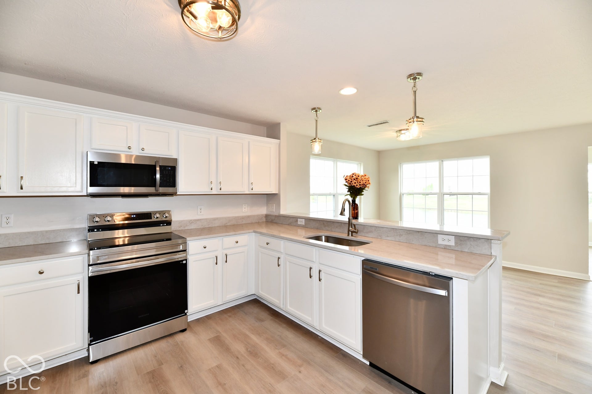 White cabinetry, stainless steel appliances, light-toned countertops, wood-finish flooring, and recessed lighting