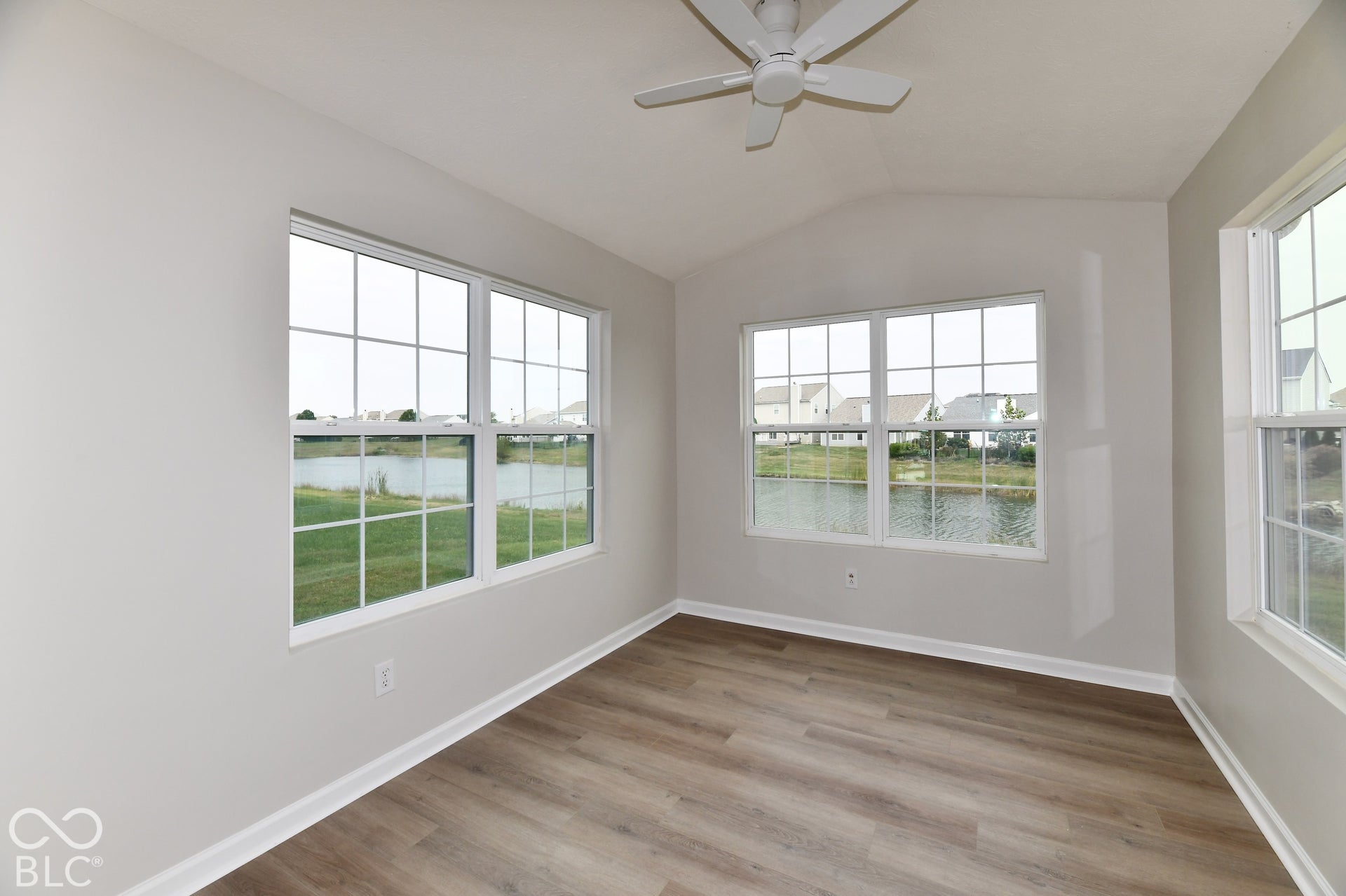 Vaulted ceiling with a ceiling fan, multiple windows with grid patterns, wood-finish flooring, and white trim
