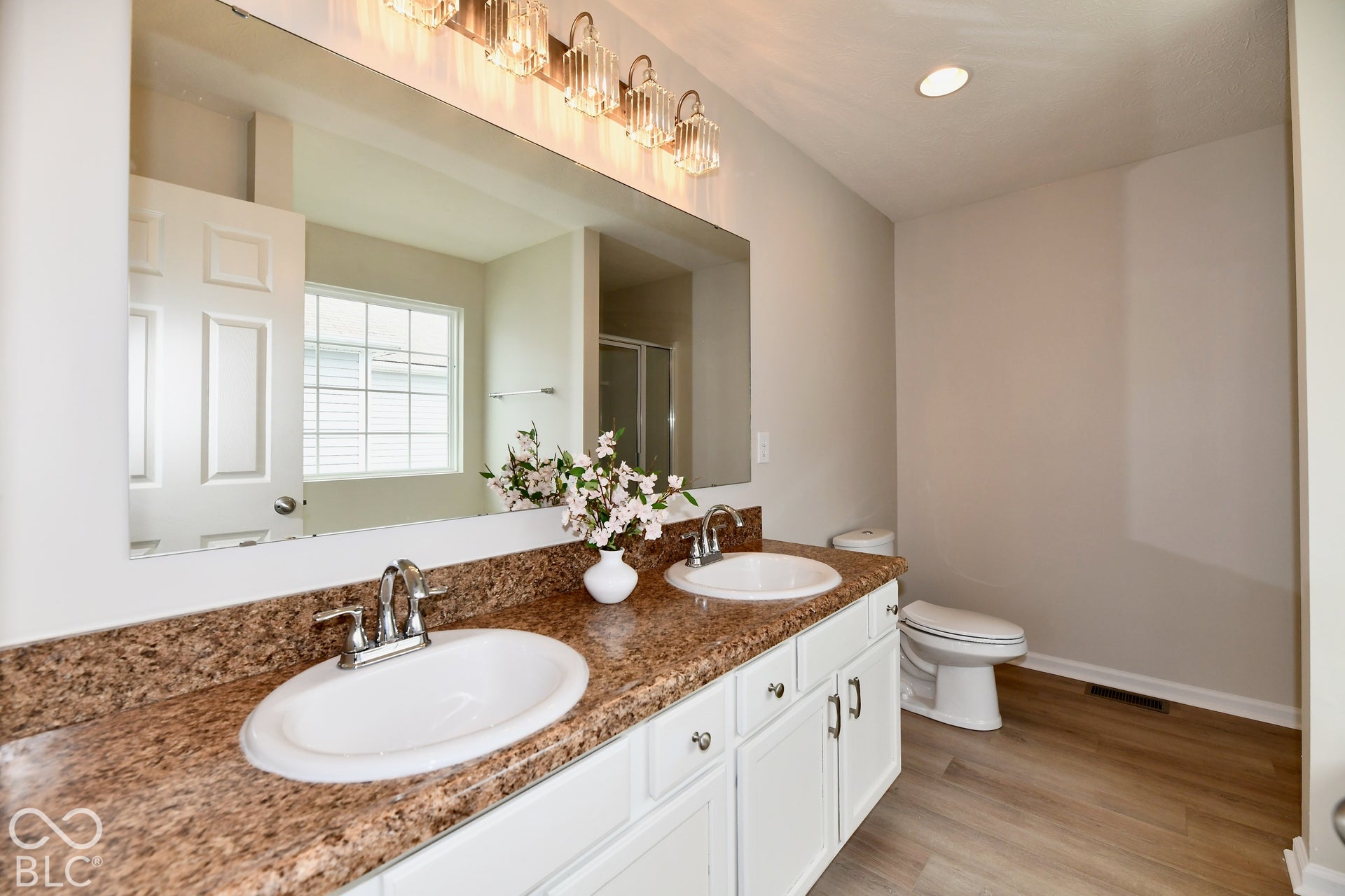 Double vanity with undermount sinks, brown-toned countertop, white cabinetry, and wood-finish flooring