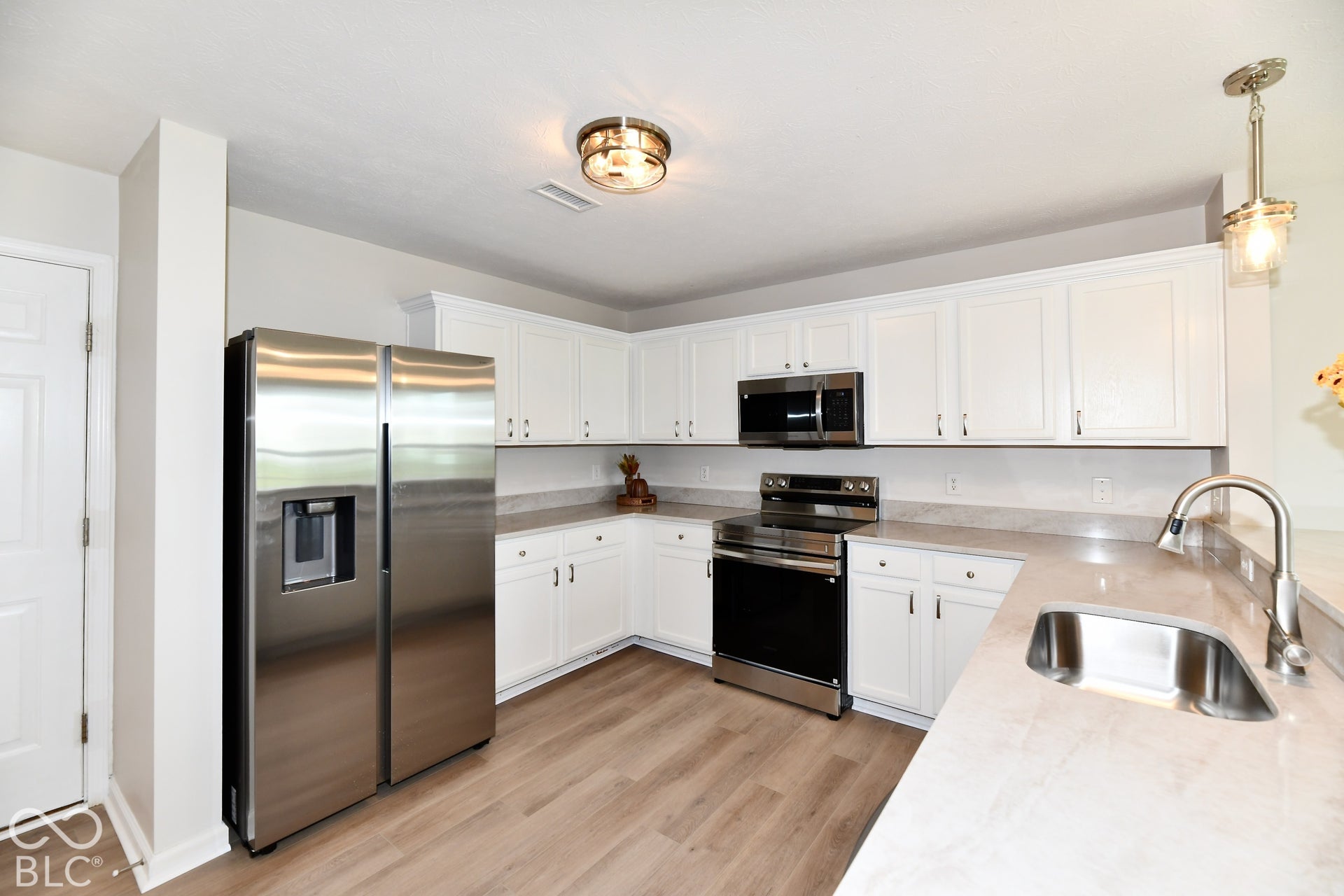 White cabinetry with brushed nickel hardware, stainless steel appliances, wood-finish flooring, and light-toned countertops