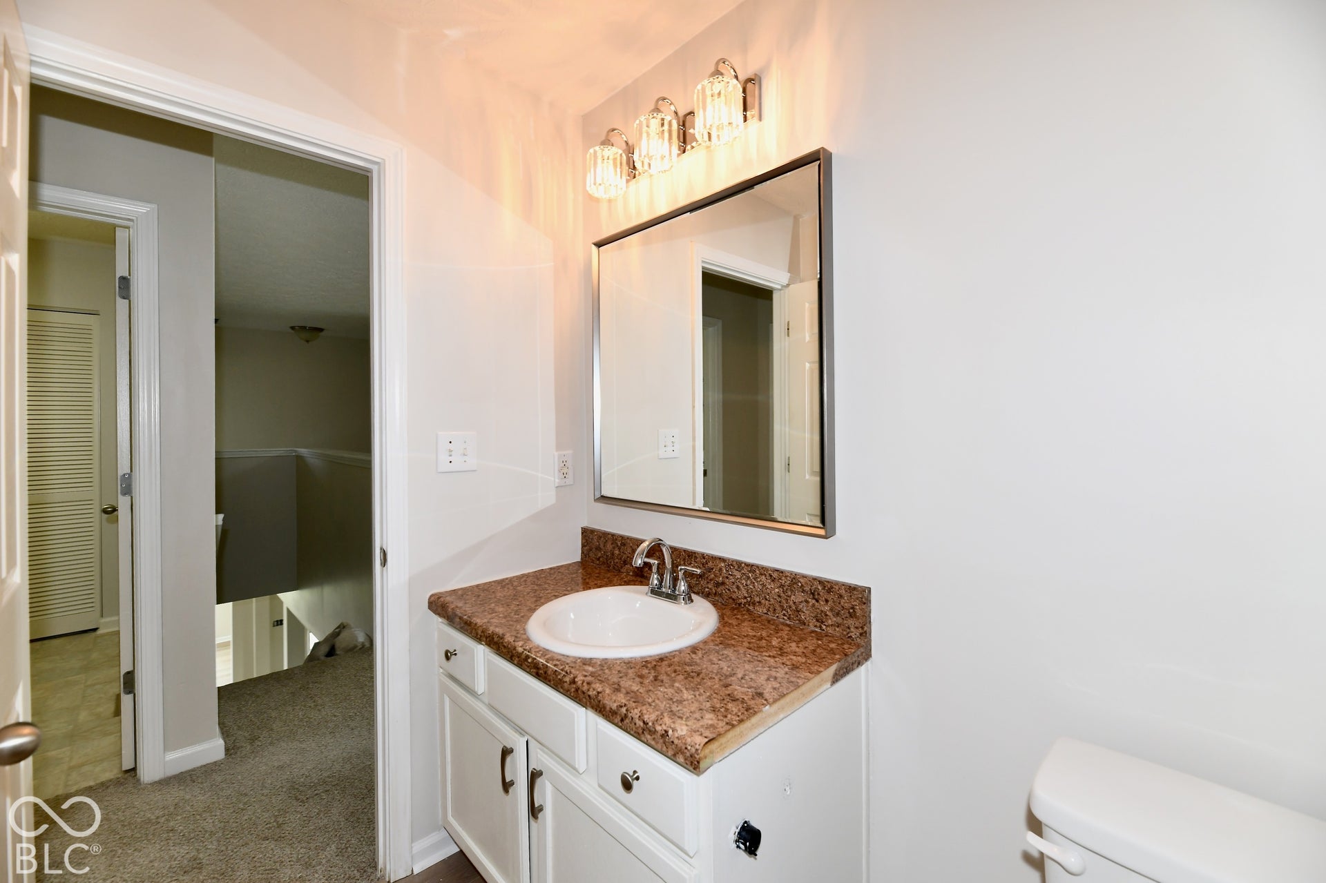 White vanity with a drop-in sink, chrome faucet, and a brown speckled countertop