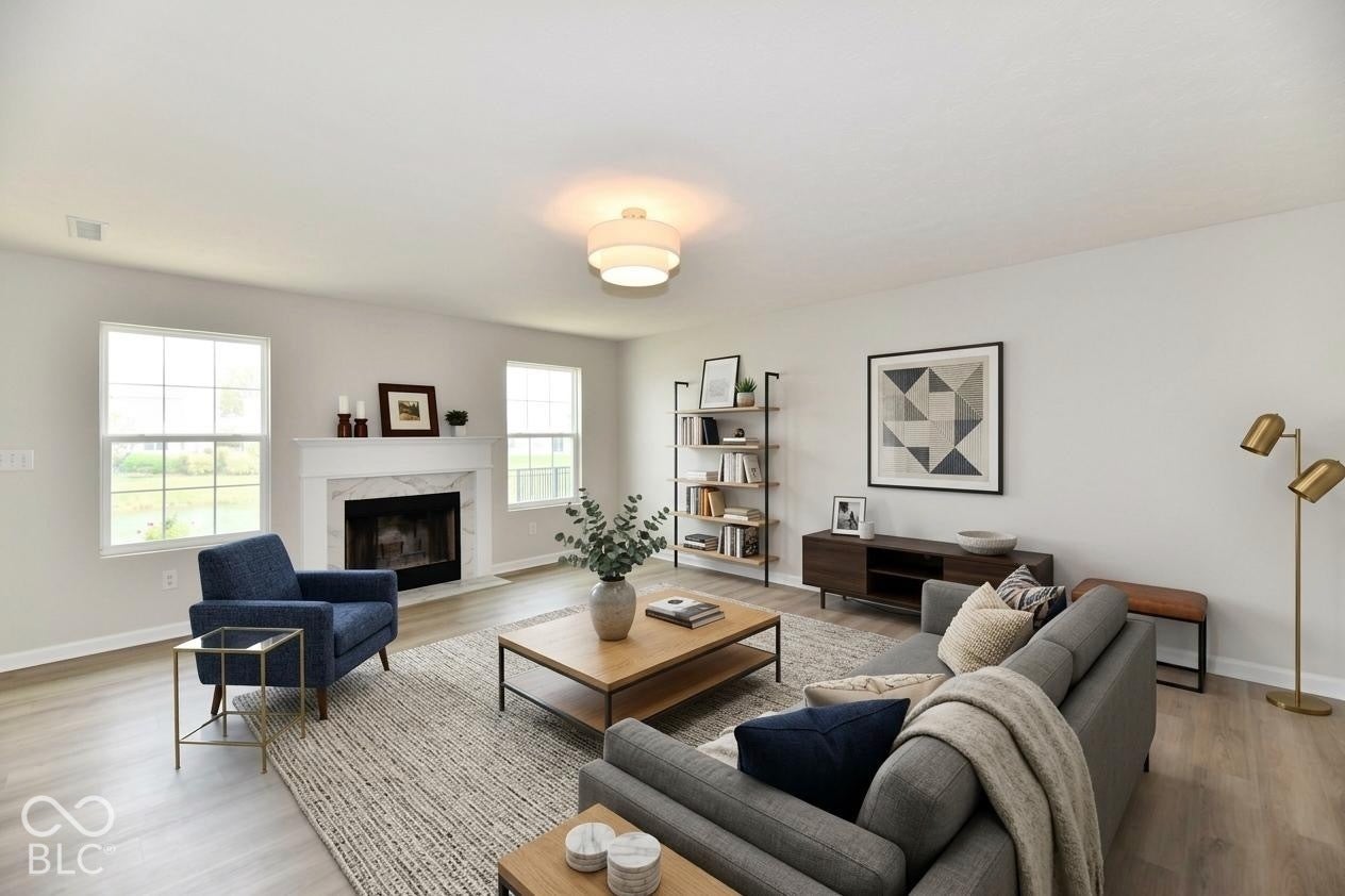 Virtually Altered - Spacious living area featuring light wood-finish flooring, a white mantel fireplace with a dark hearth, and multiple windows