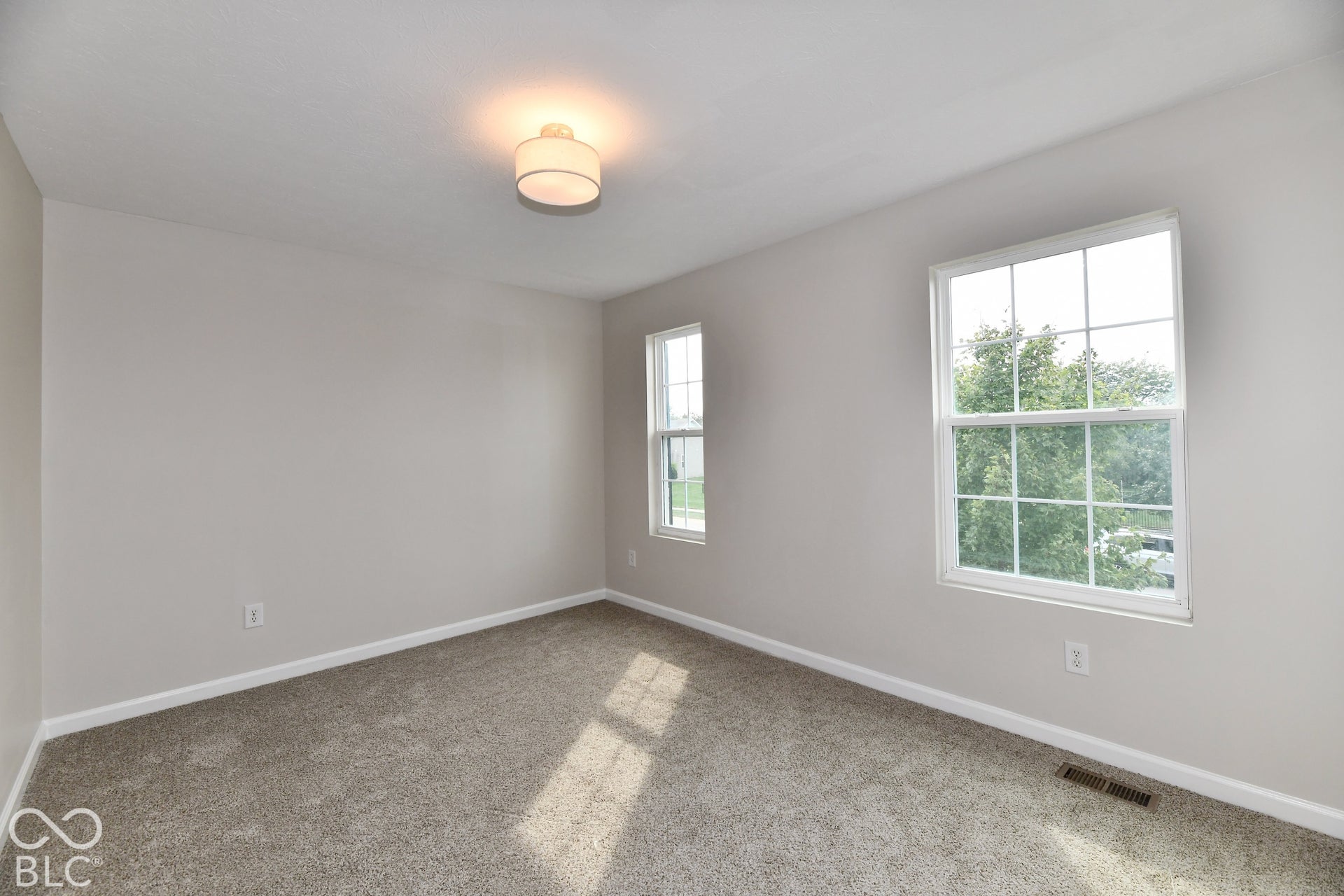 One of three bedrooms in neutral wall tones, ceiling-mounted light fixture, two windows, and gray carpet flooring