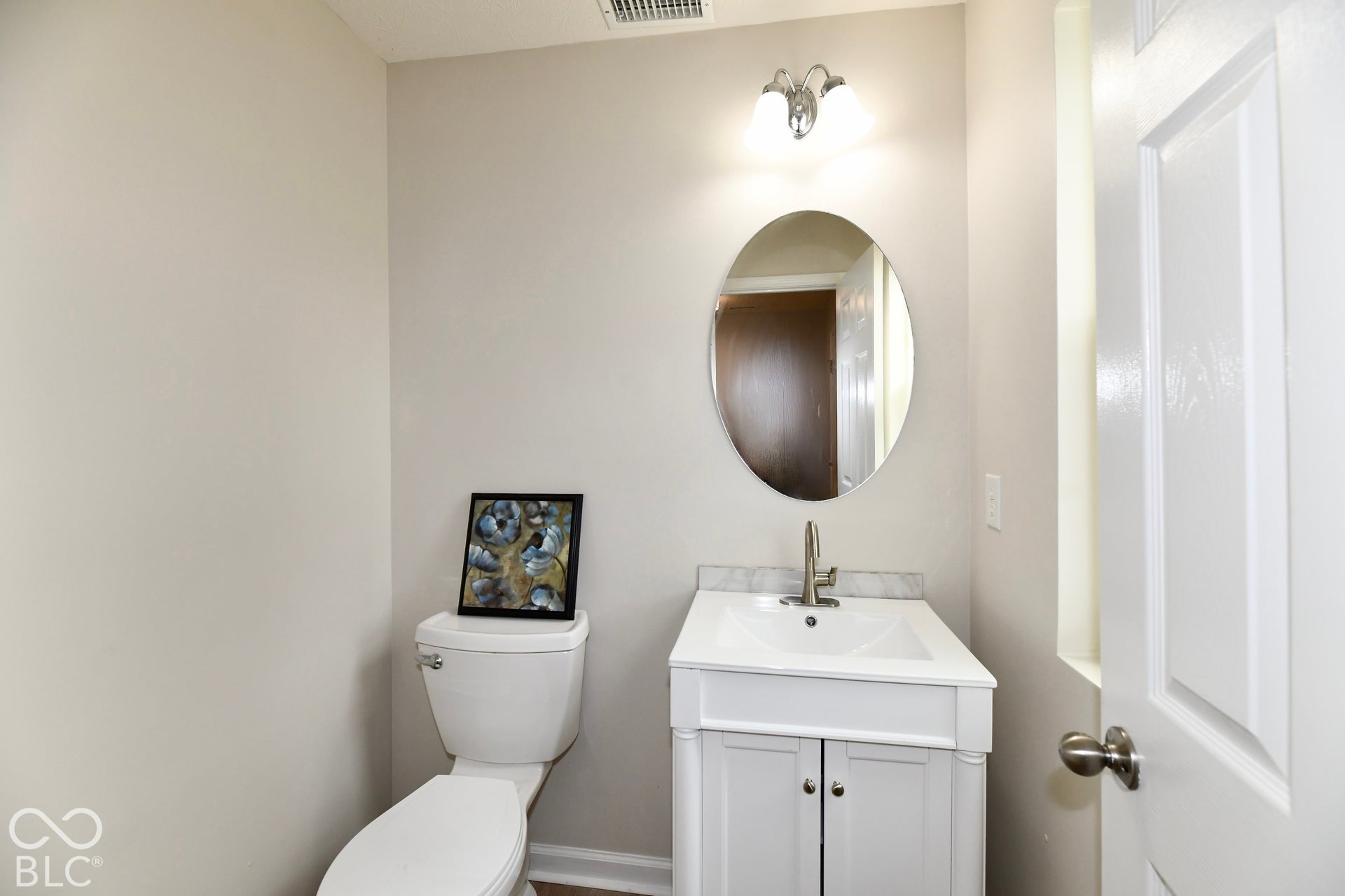 White vanity with integrated sink, brushed nickel faucet, oval mirror, and overhead vanity lighting