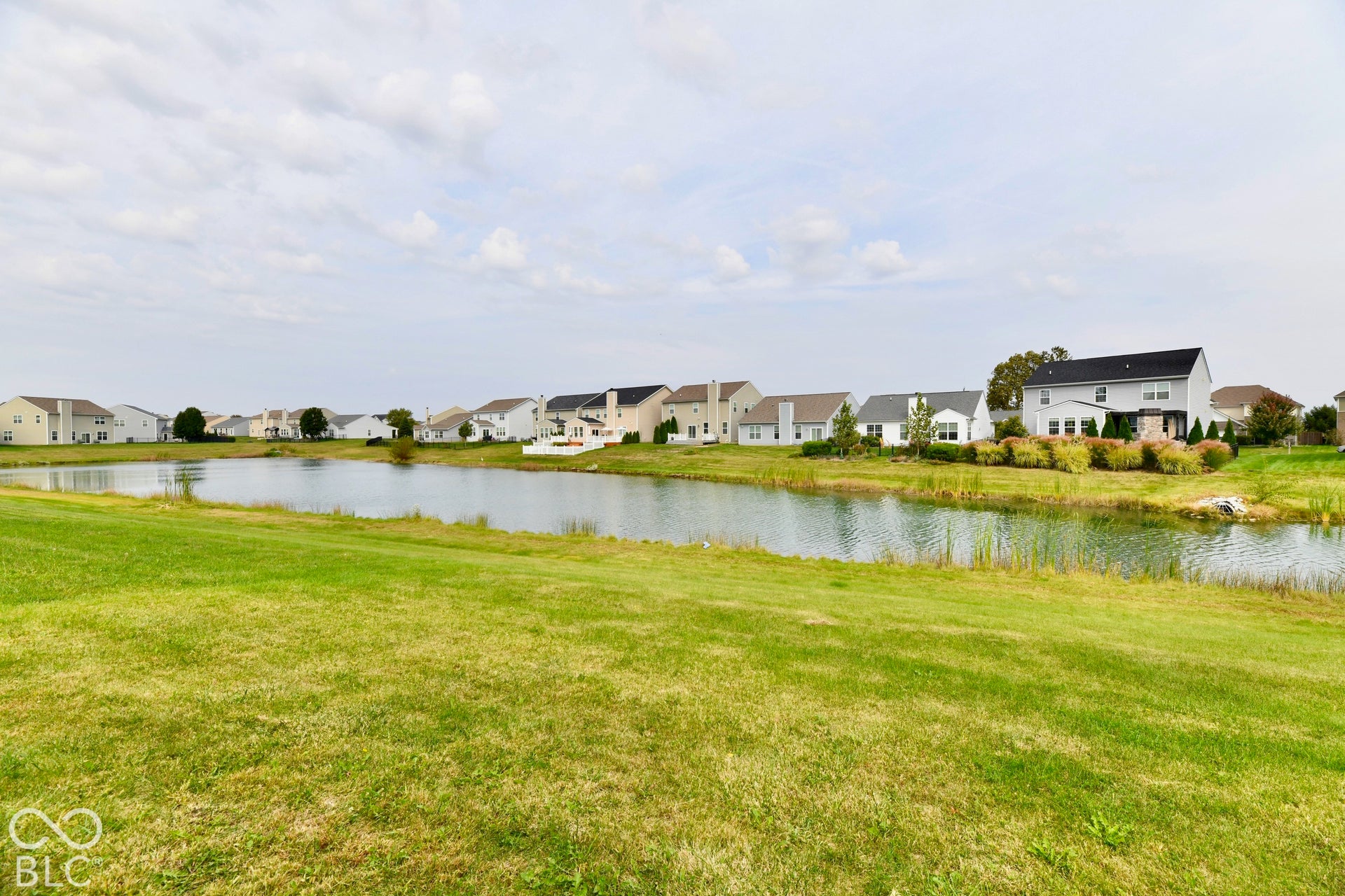 Expansive green space featuring a pond and distant residences