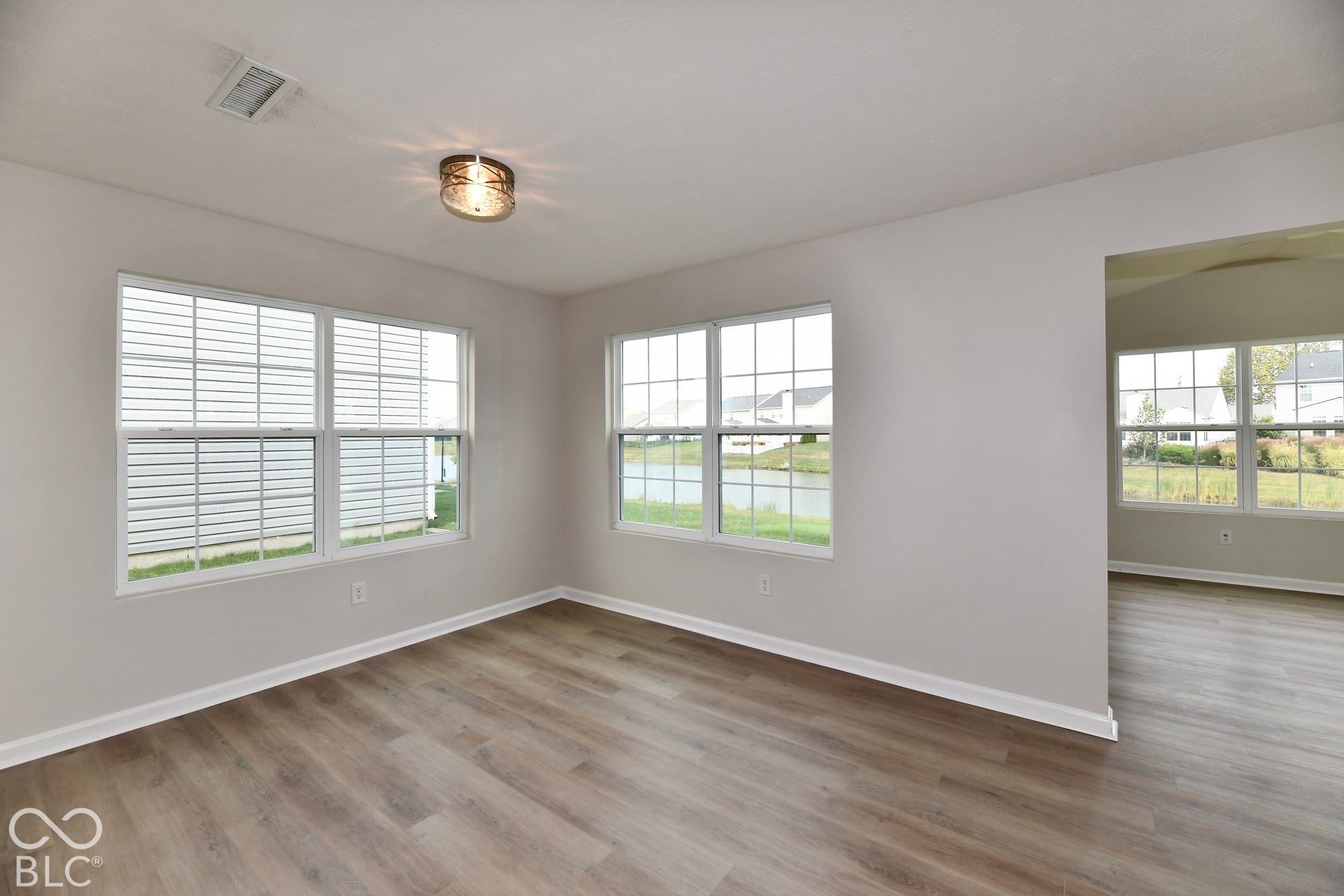 Wood-finish flooring throughout, multiple windows, white baseboards, and a semi-flush ceiling light fixture