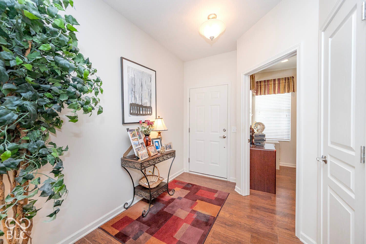 Entryway featuring laminate flooring, a flush mount ceiling light, a paneled door with brushed nickel hardware, and a doorway to the den, which is currently used as an office.