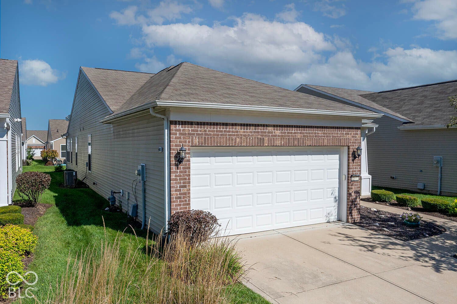view of the garage and the west side of the home. Brick facade with a white garage door, concrete driveway, and exterior lighting fixtures