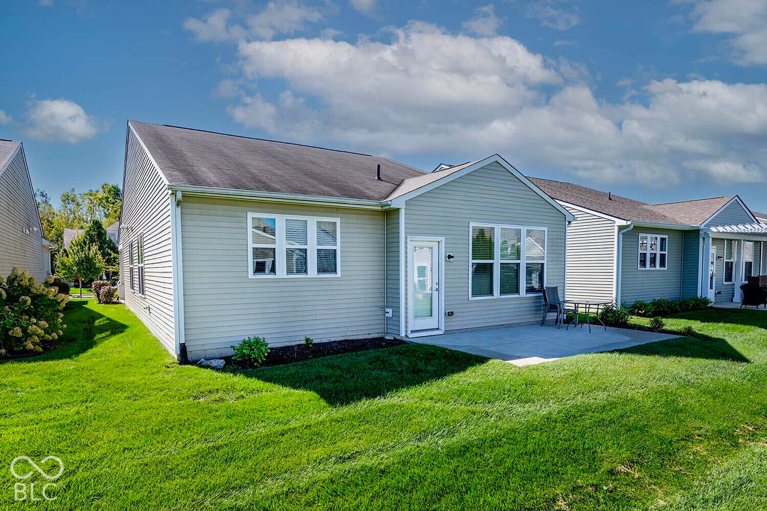 Expansive rear lawn area with a concrete patio, exterior siding, and multiple windows