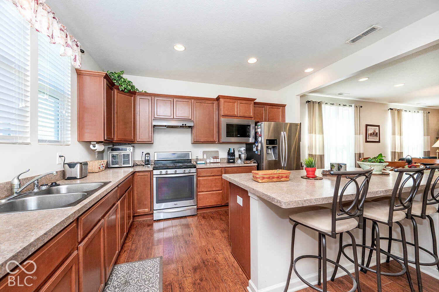 Kitchen featuring wood-finish cabinetry, stainless steel appliances, a double basin sink, recessed lighting, and a breakfast bar with seating