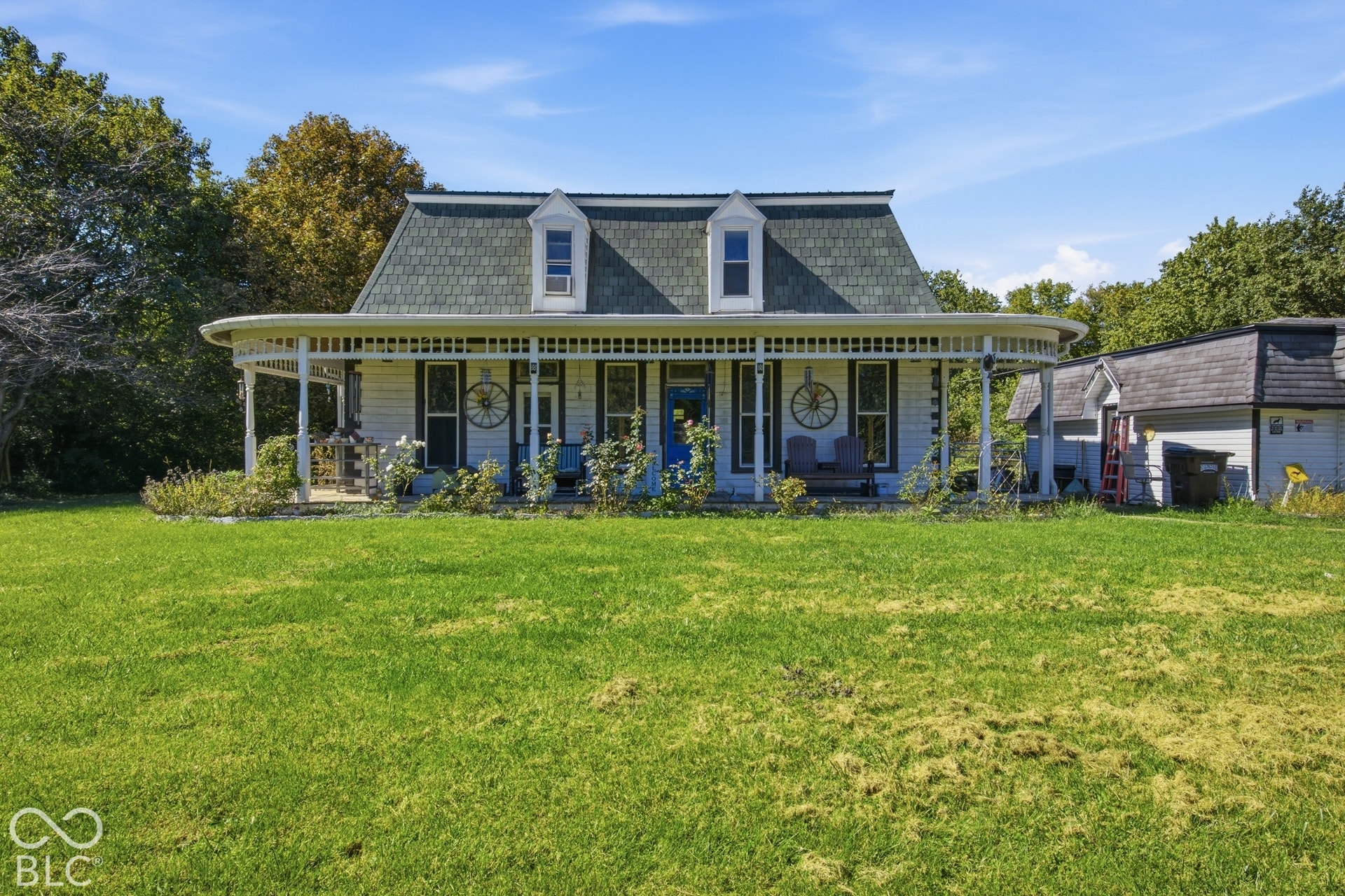 Victorian-style residence featuring a wrap-around porch, dormer windows, a prominent gable roof, and an adjacent outbuilding