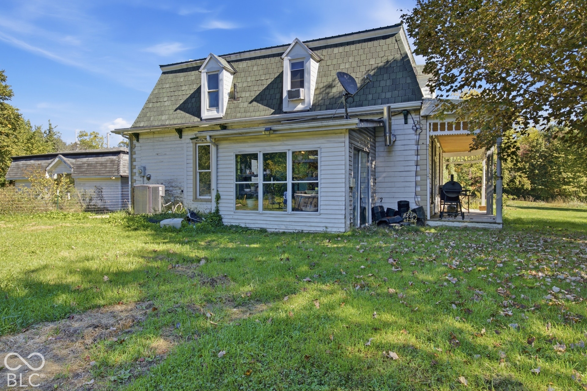 Gambrel roofline with dormer windows, white siding exterior, large multi-pane windows, covered porch, and expansive grassy area