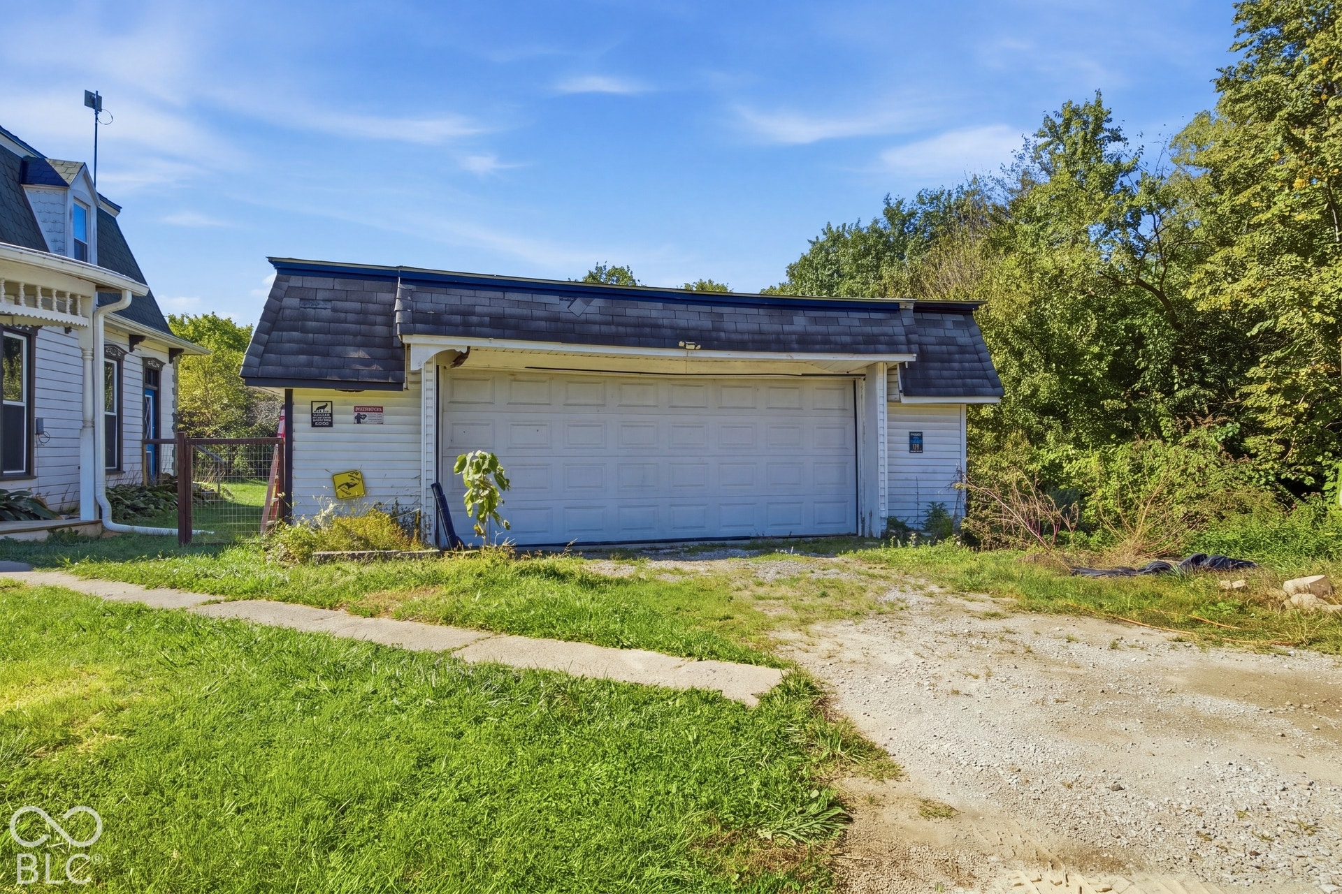 Virtually Altered - Detached garage with white composite siding, oversized white paneled garage door, and dark asphalt shingle roofing