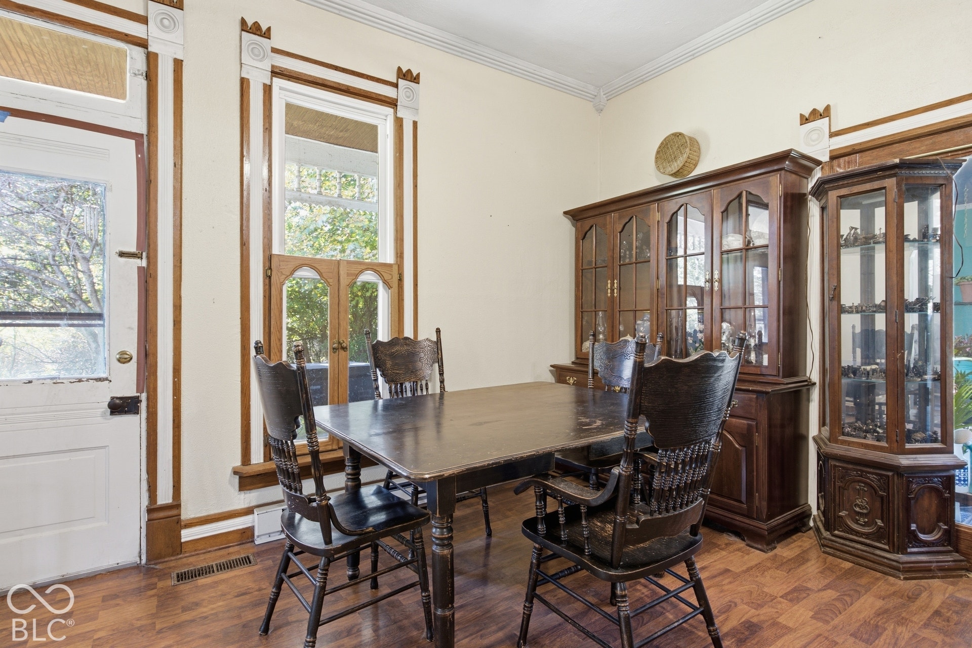 Elegant formal dining room showcasing rich wood-finish flooring, substantial wood cabinetry with glass-front display doors, and multiple tall windows with wood trim framing natural light