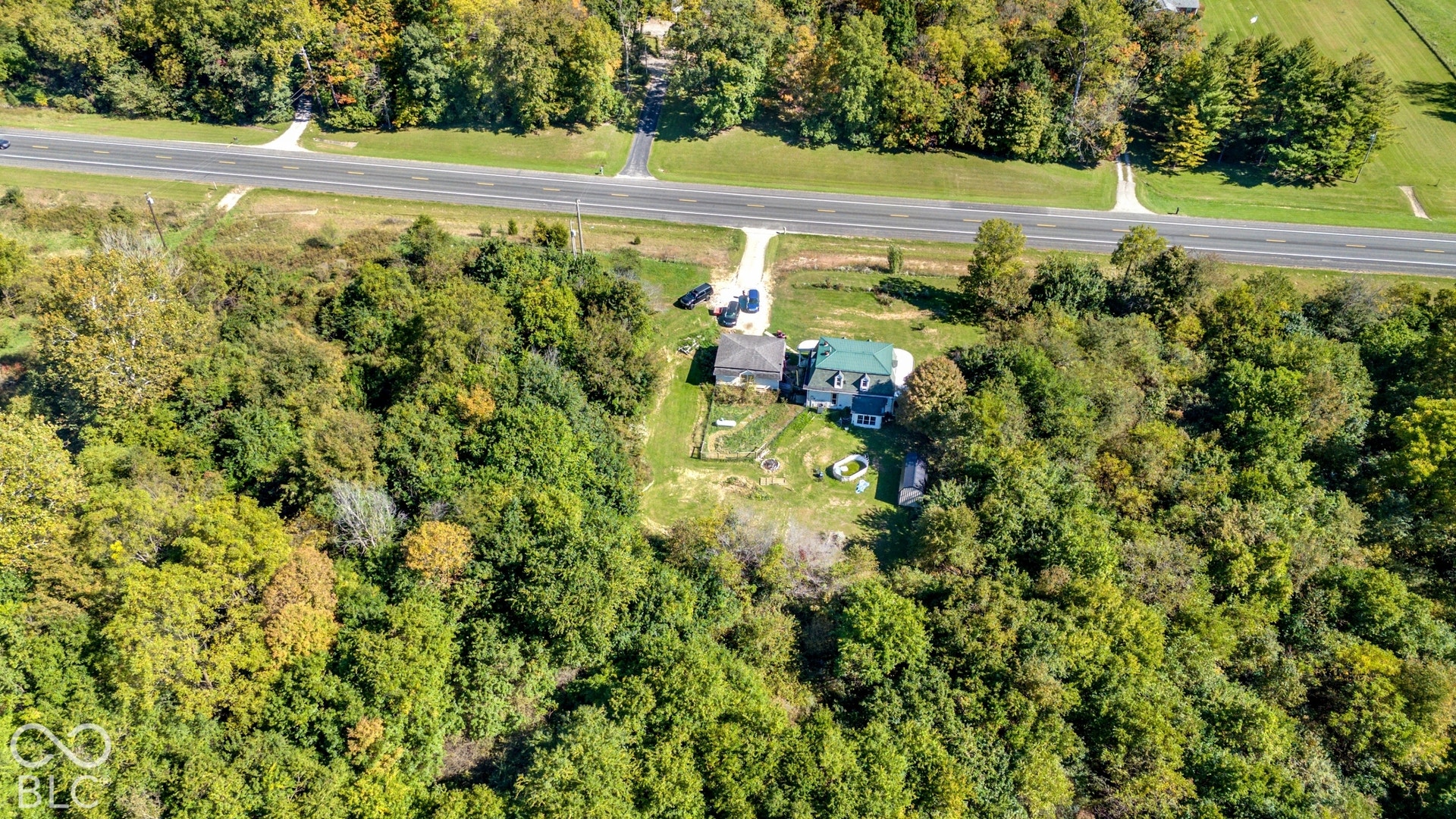 Rural setting with a private drive, surrounding mature trees, and a visible roadway