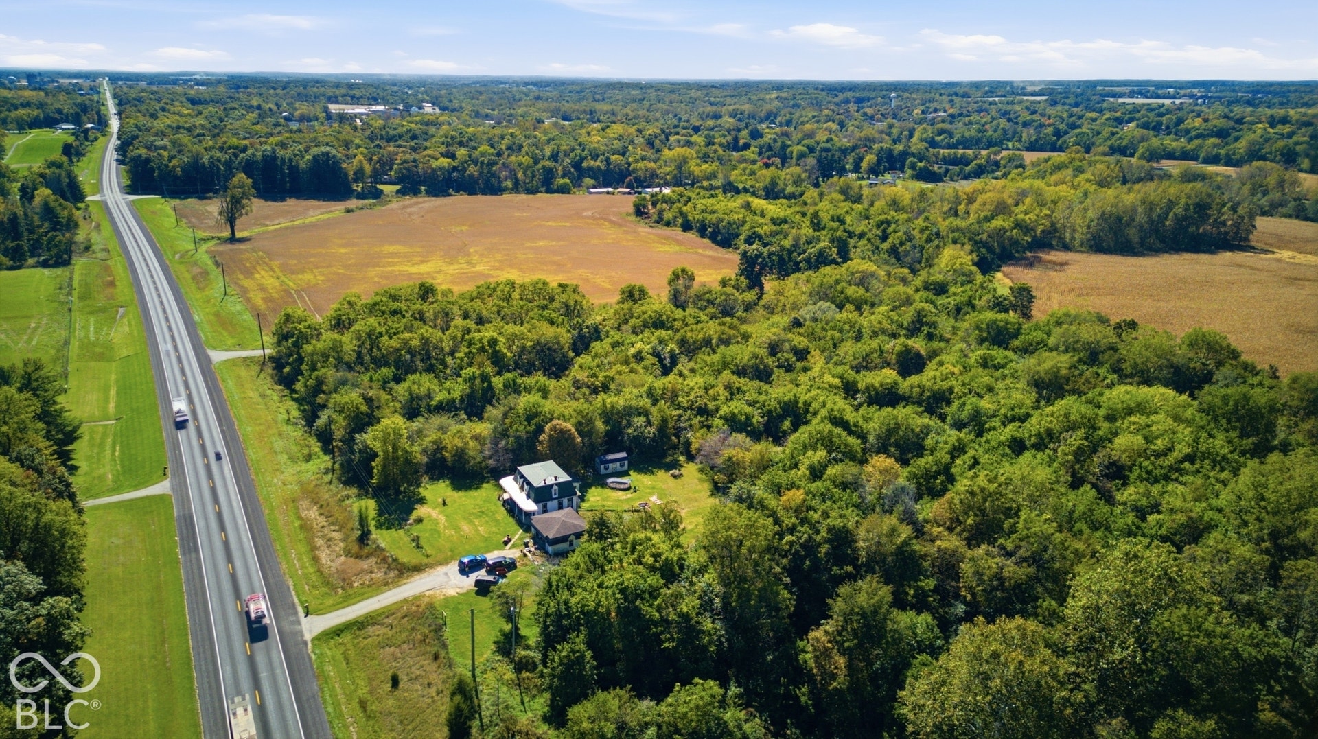 Scenic rural property featuring a substantial home nestled among mature tree coverage, with direct highway access via a dedicated driveway