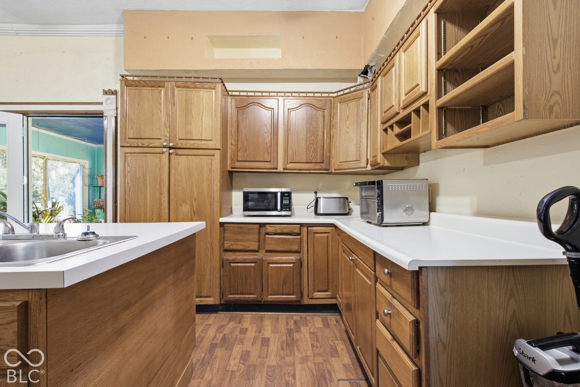 Galley-style kitchen featuring warm wood cabinetry with raised-panel doors, white countertops, wood-finish flooring, and stainless steel appliances including a microwave and cooktop