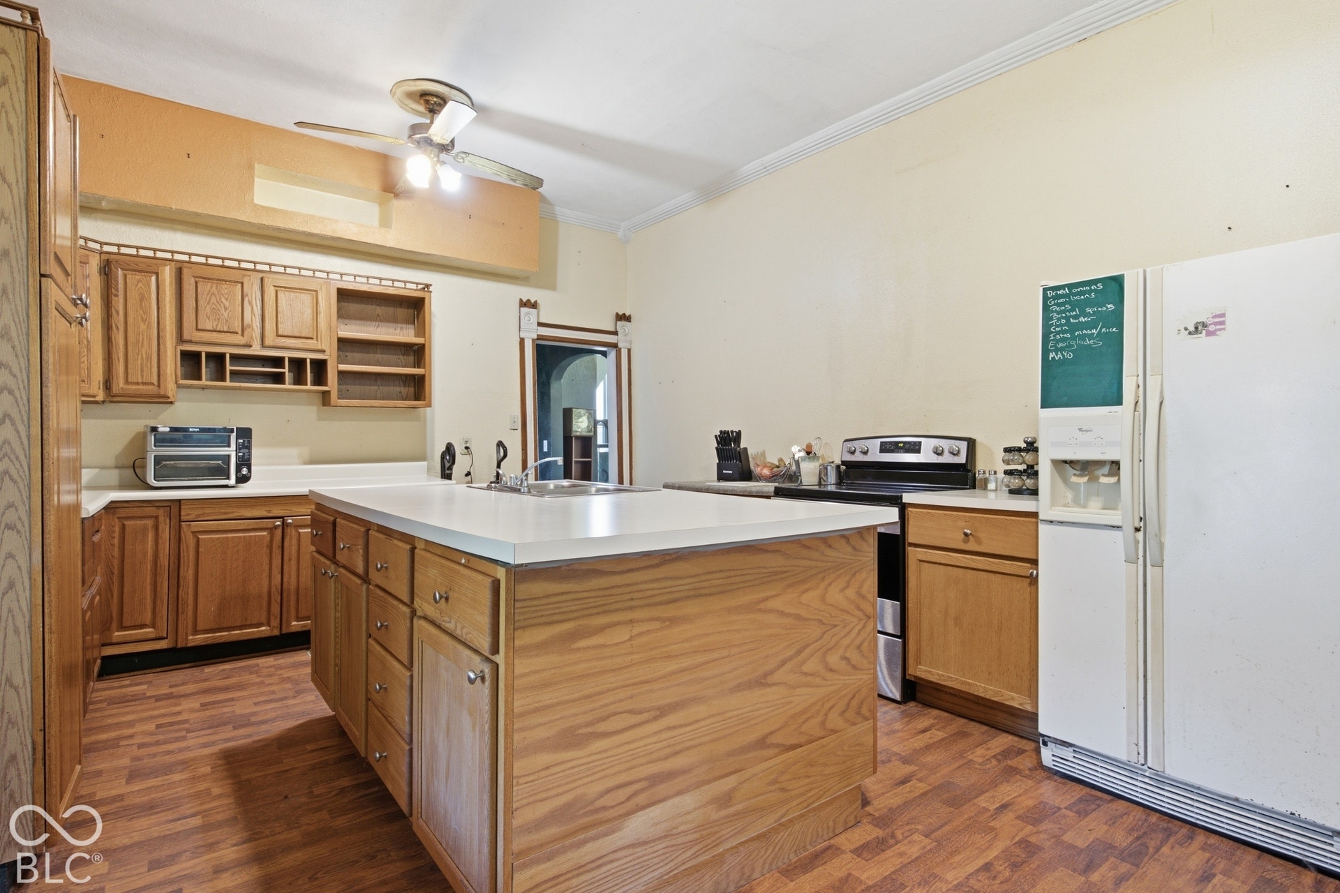 Spacious kitchen featuring wood cabinetry, a large center island with white countertop, stainless steel appliances, hardwood flooring, and ample storage throughout