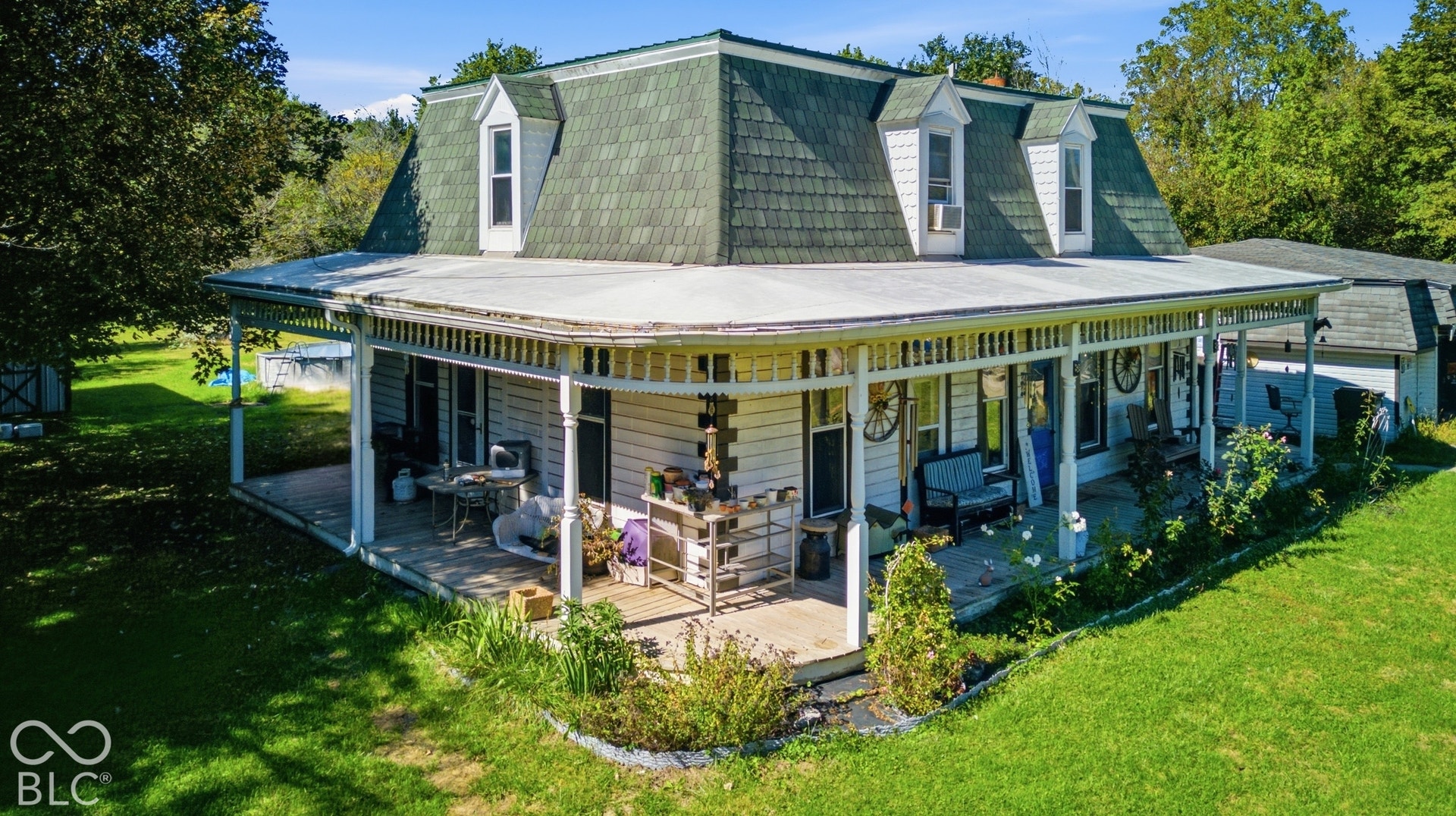 Dormer windows, wraparound porch, decorative porch columns, white siding, and green shingle roof