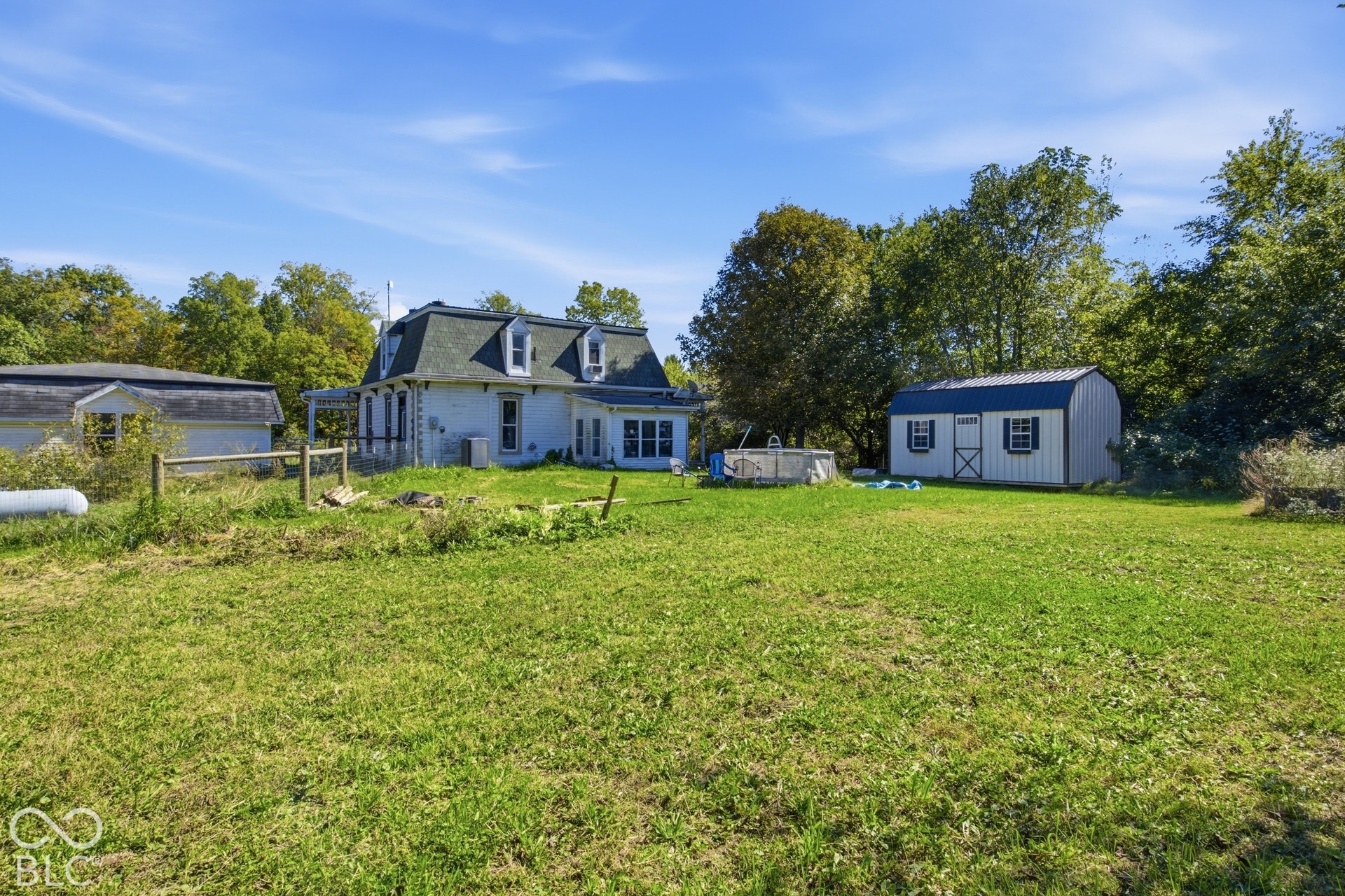 Expansive property featuring a white residence with dark roof, dormer windows, a detached garage, and a separate shed with a dark roof