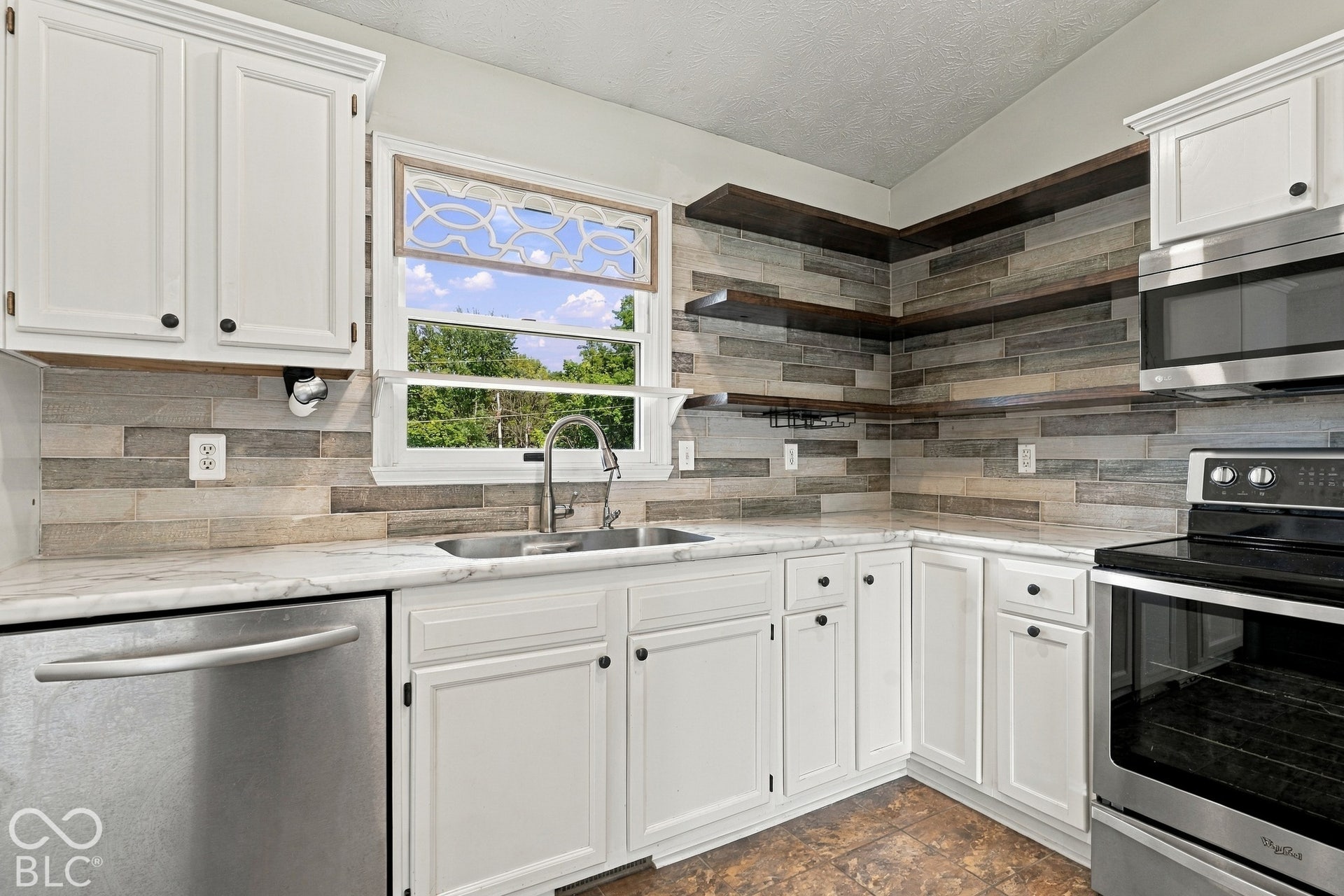 White cabinetry with black hardware, an undermount double basin sink, stainless steel appliances, and wood-look tile backsplash