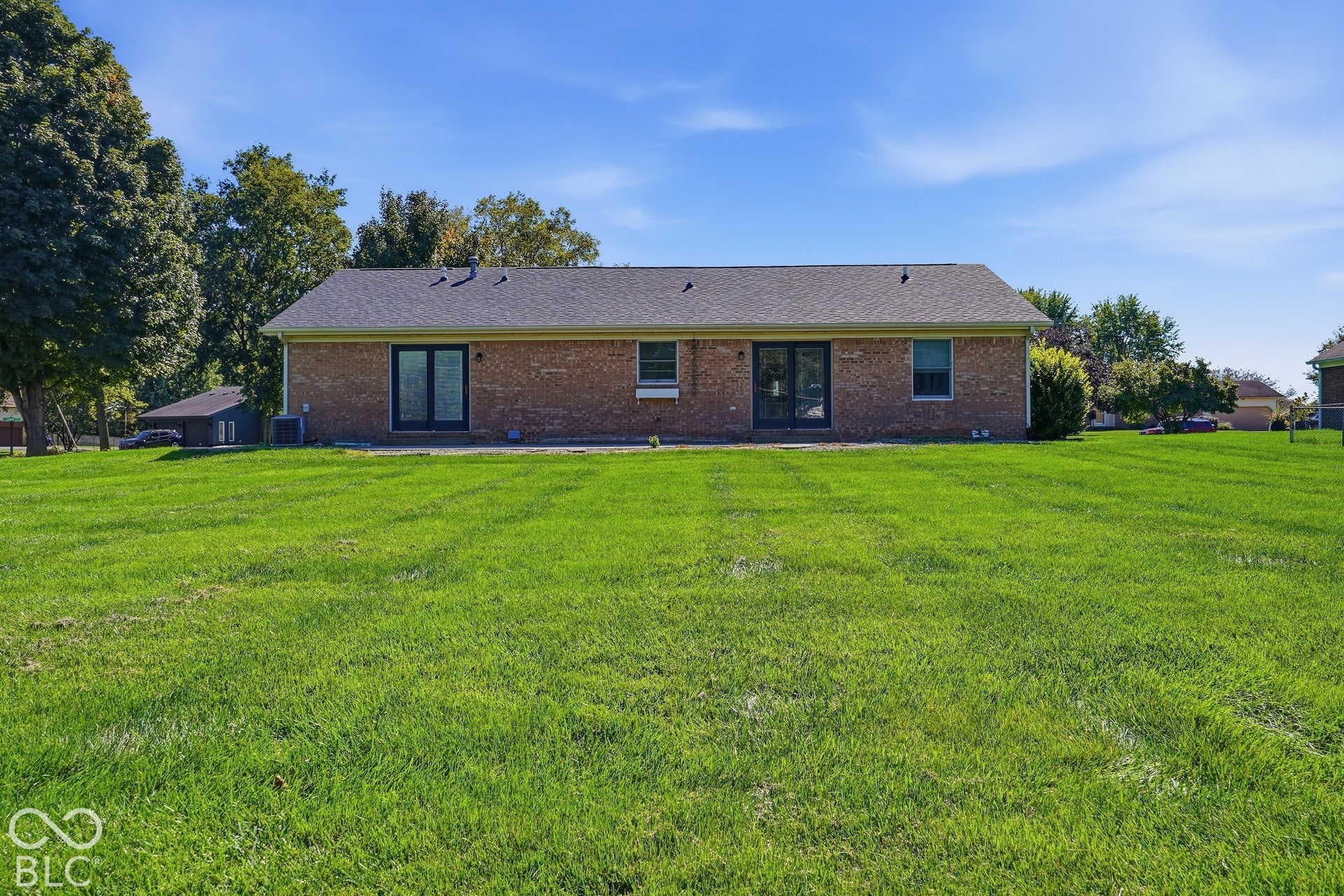 Expansive green lawn with mature perimeter trees, brick exterior, and two sets of black-framed patio doors