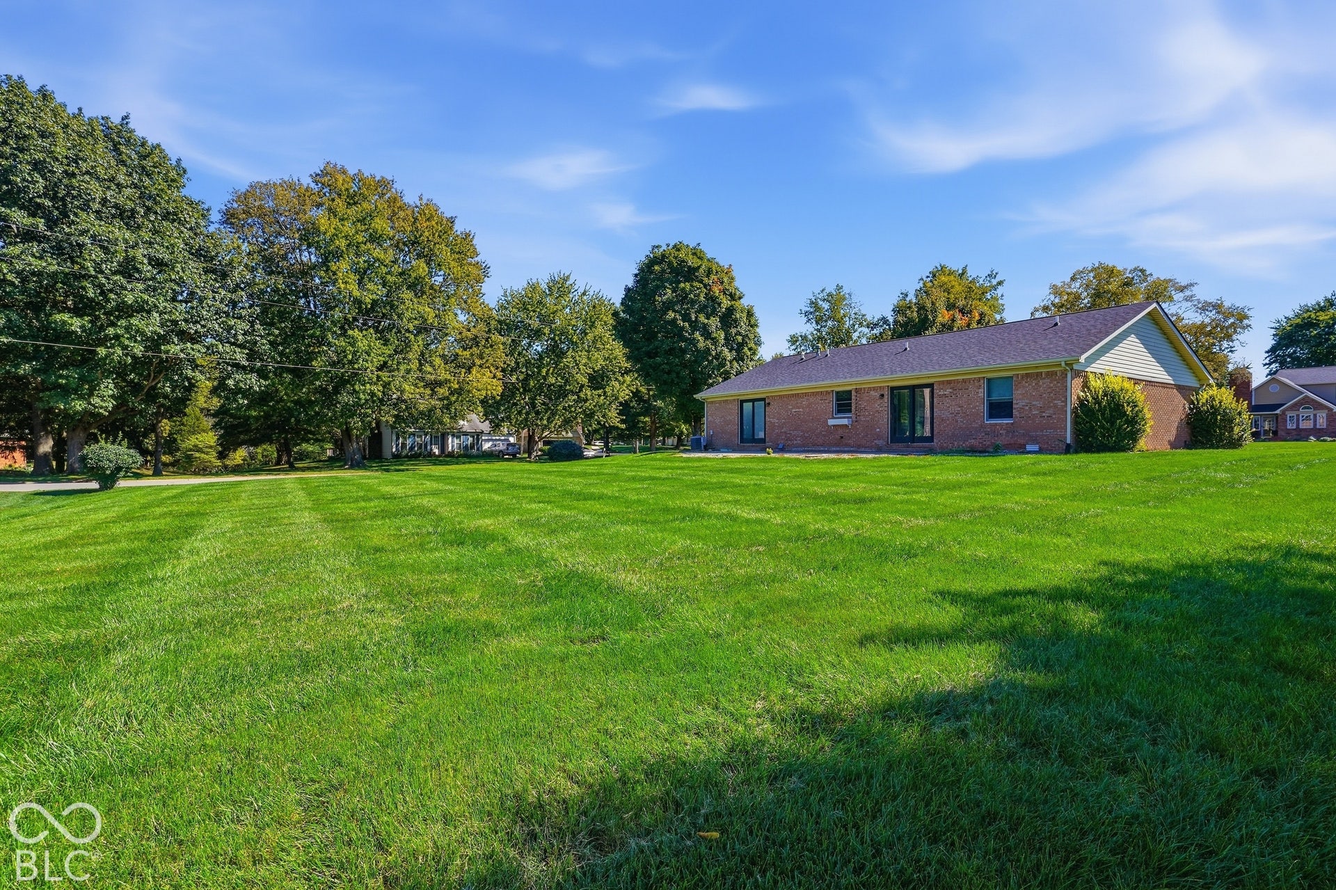 Expansive green lawn, mature trees, brick exterior, dark-toned roof, and rear patio doors