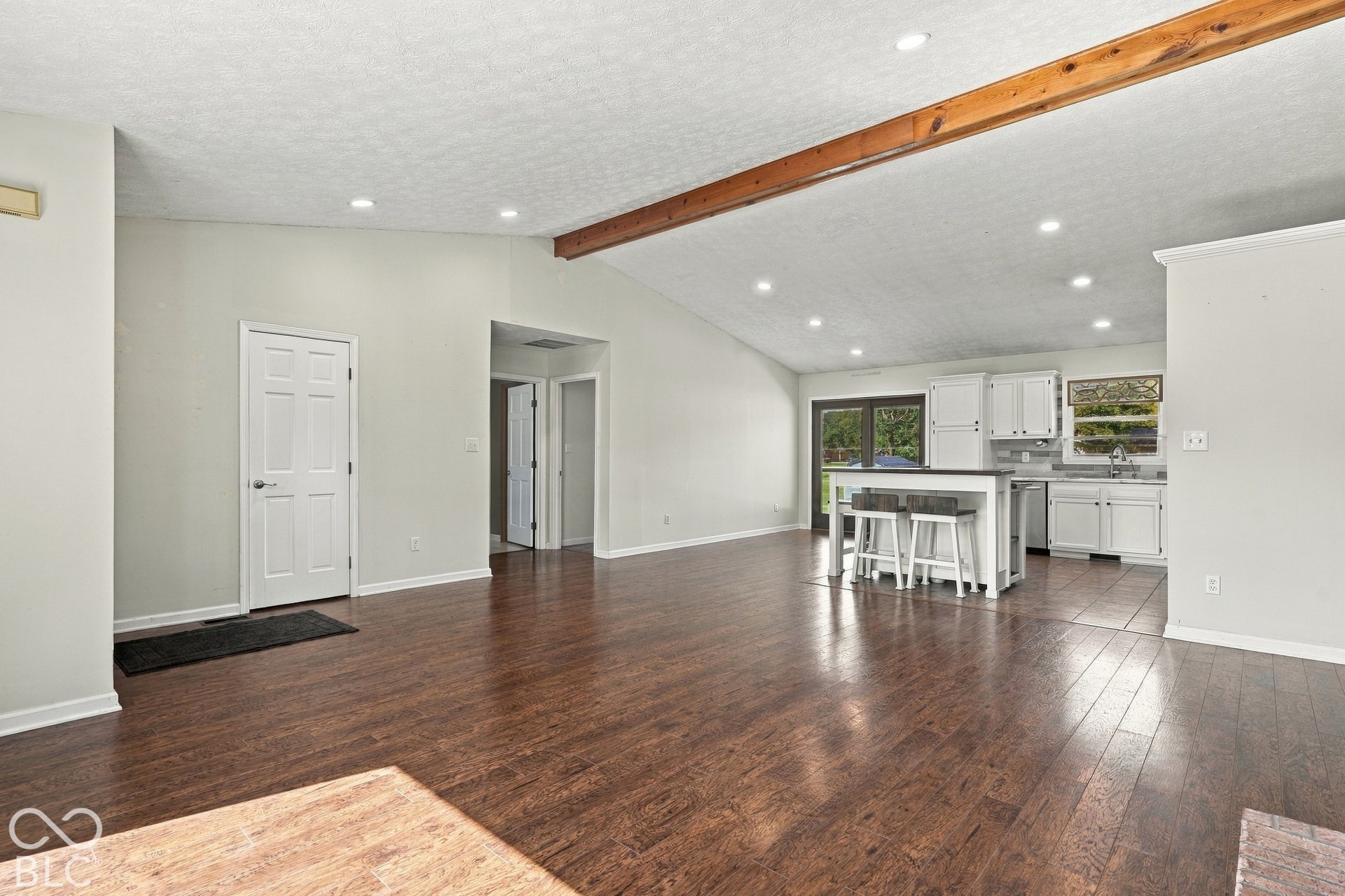 Vaulted ceiling with exposed wood beam, recessed lighting, wood-finish flooring, white kitchen cabinetry, and a kitchen island with seating