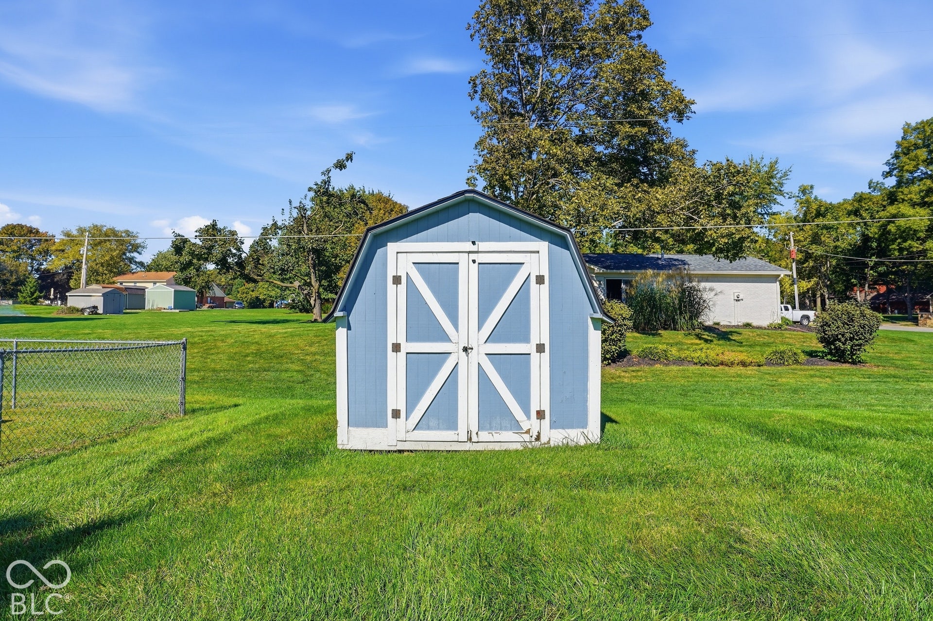 Blue utility shed with a gambrel roof and white barn doors