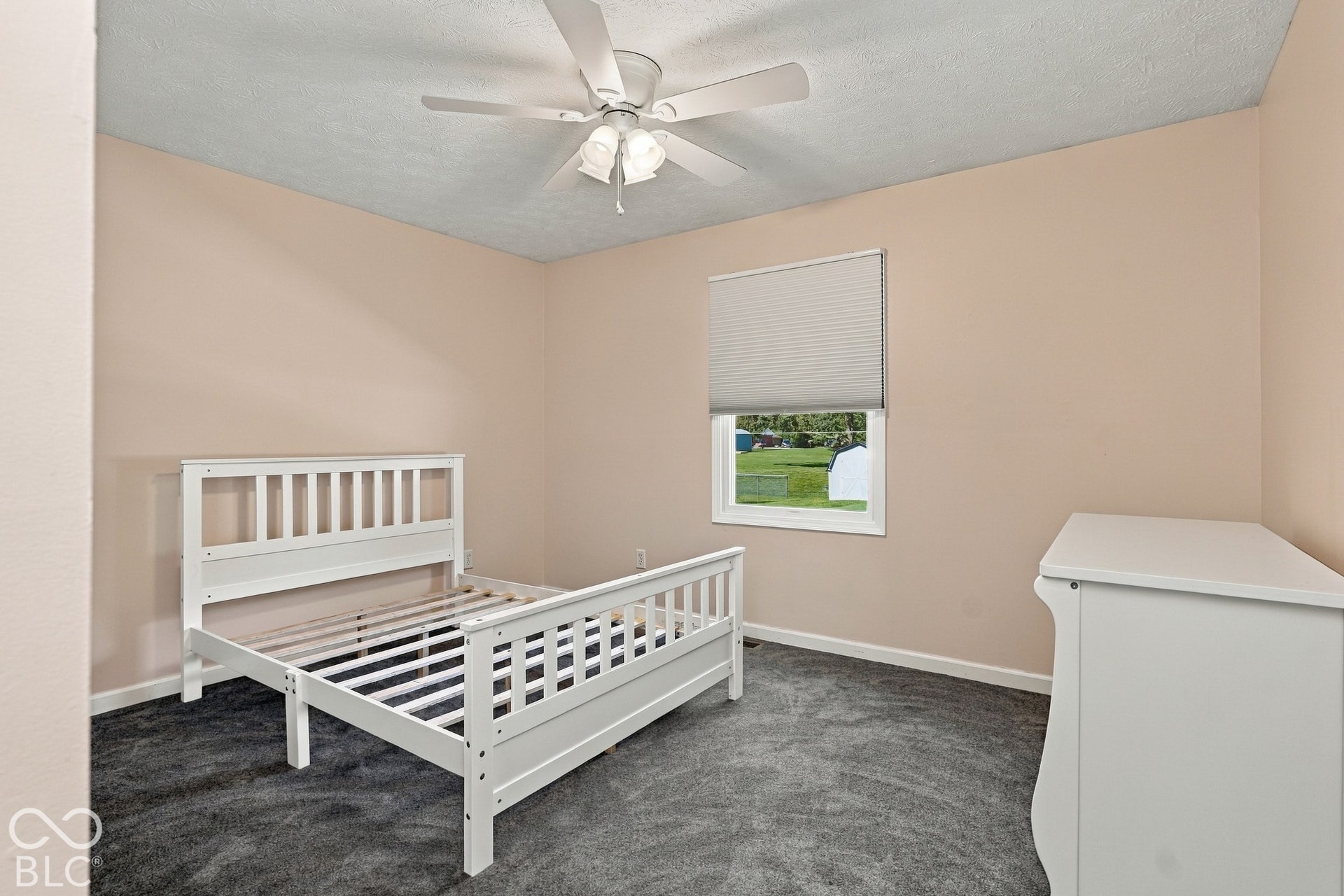 Plush gray carpeting, a bright window with cellular shades, and a ceiling fan with integrated lighting