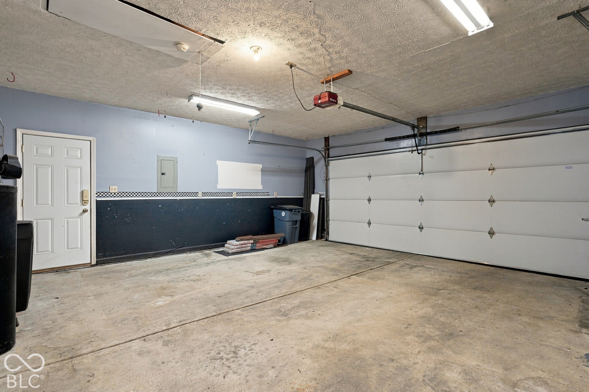 Attached garage with a panel garage door, concrete flooring, and exposed ceiling joists
