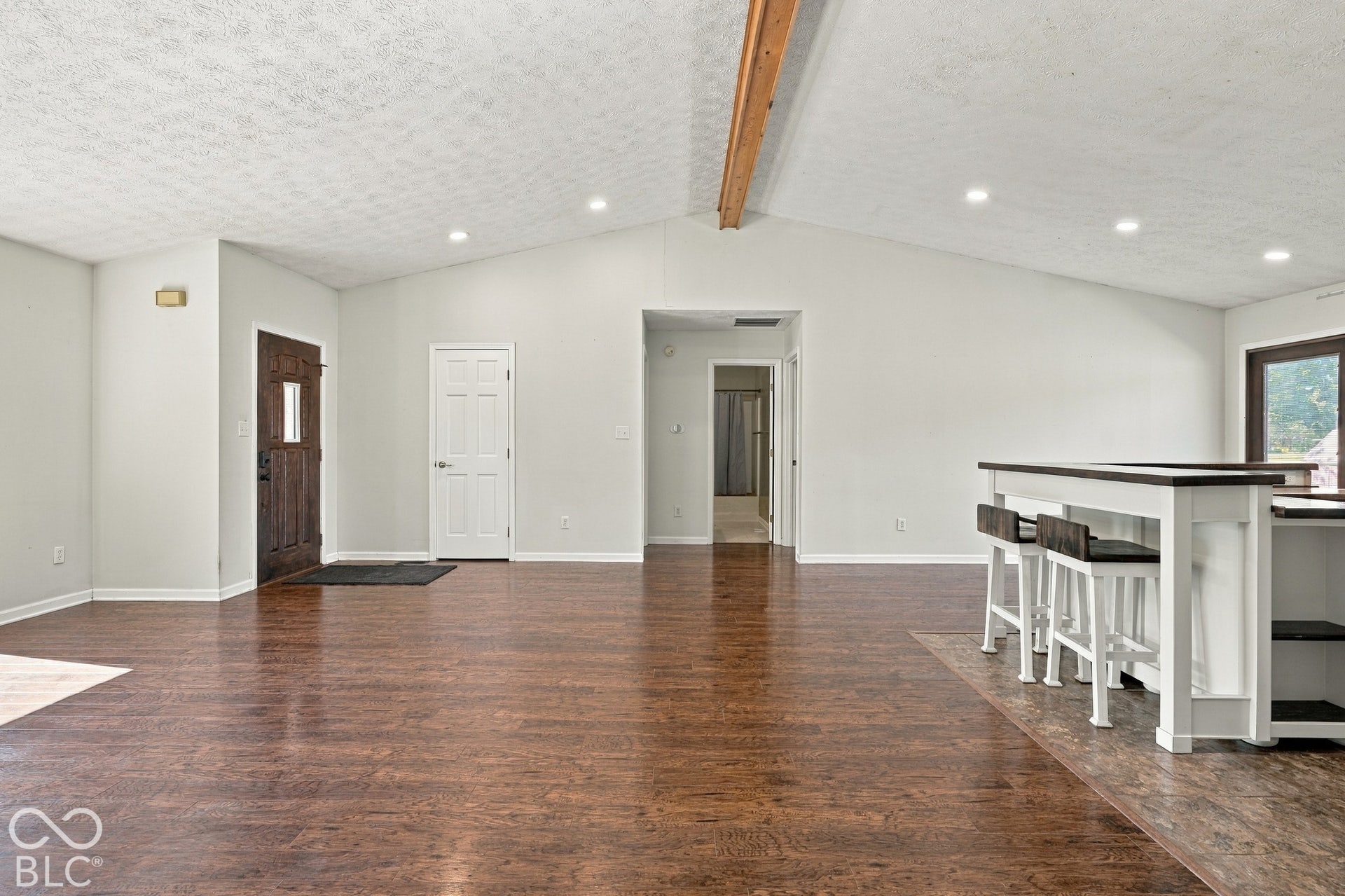 Vaulted ceiling with exposed wood beam, recessed lighting, wood-finish flooring, and a built-in kitchen island with seating