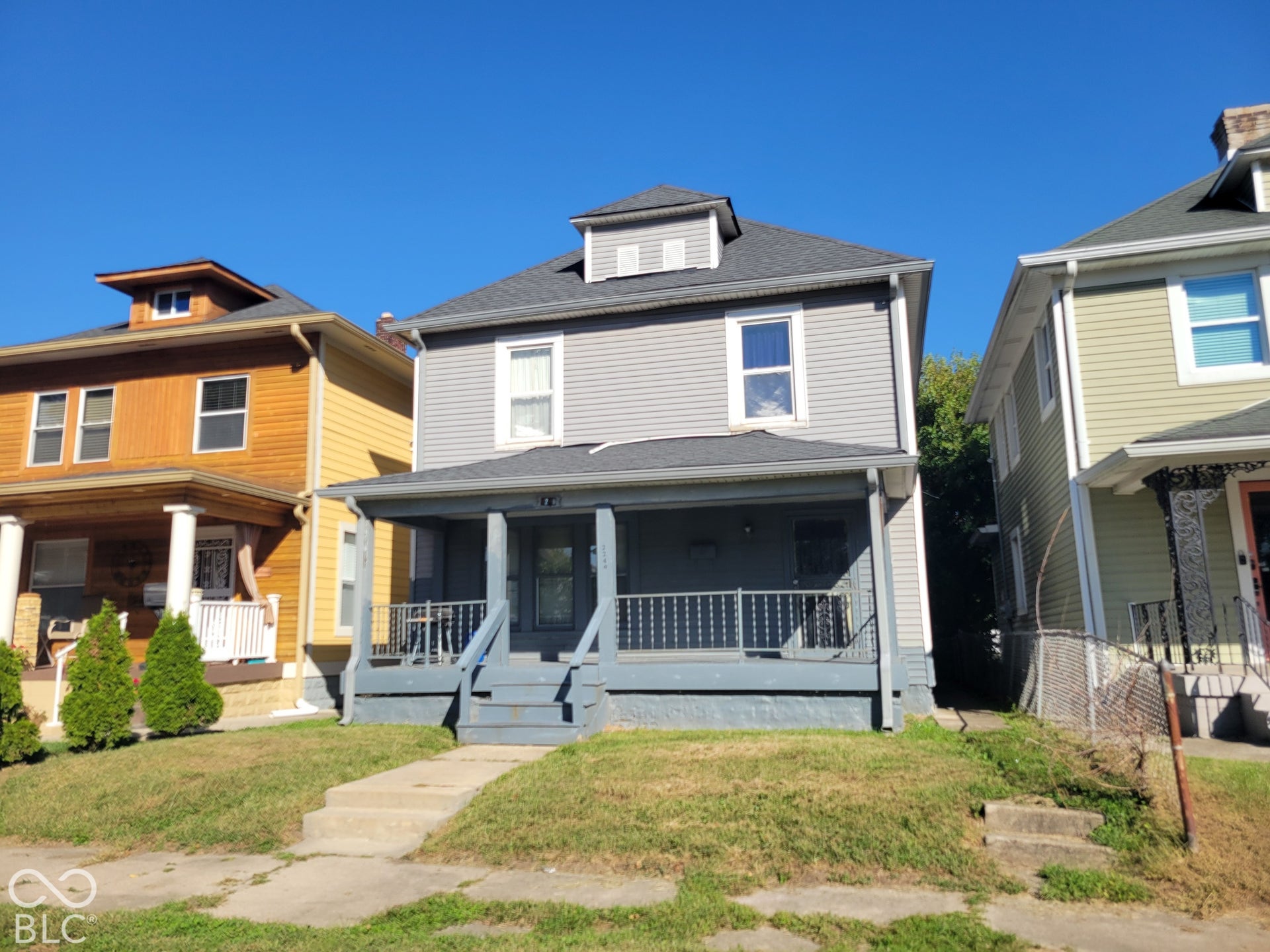 Two-story residence featuring grey siding, a covered front porch with white railings, and a dormer window