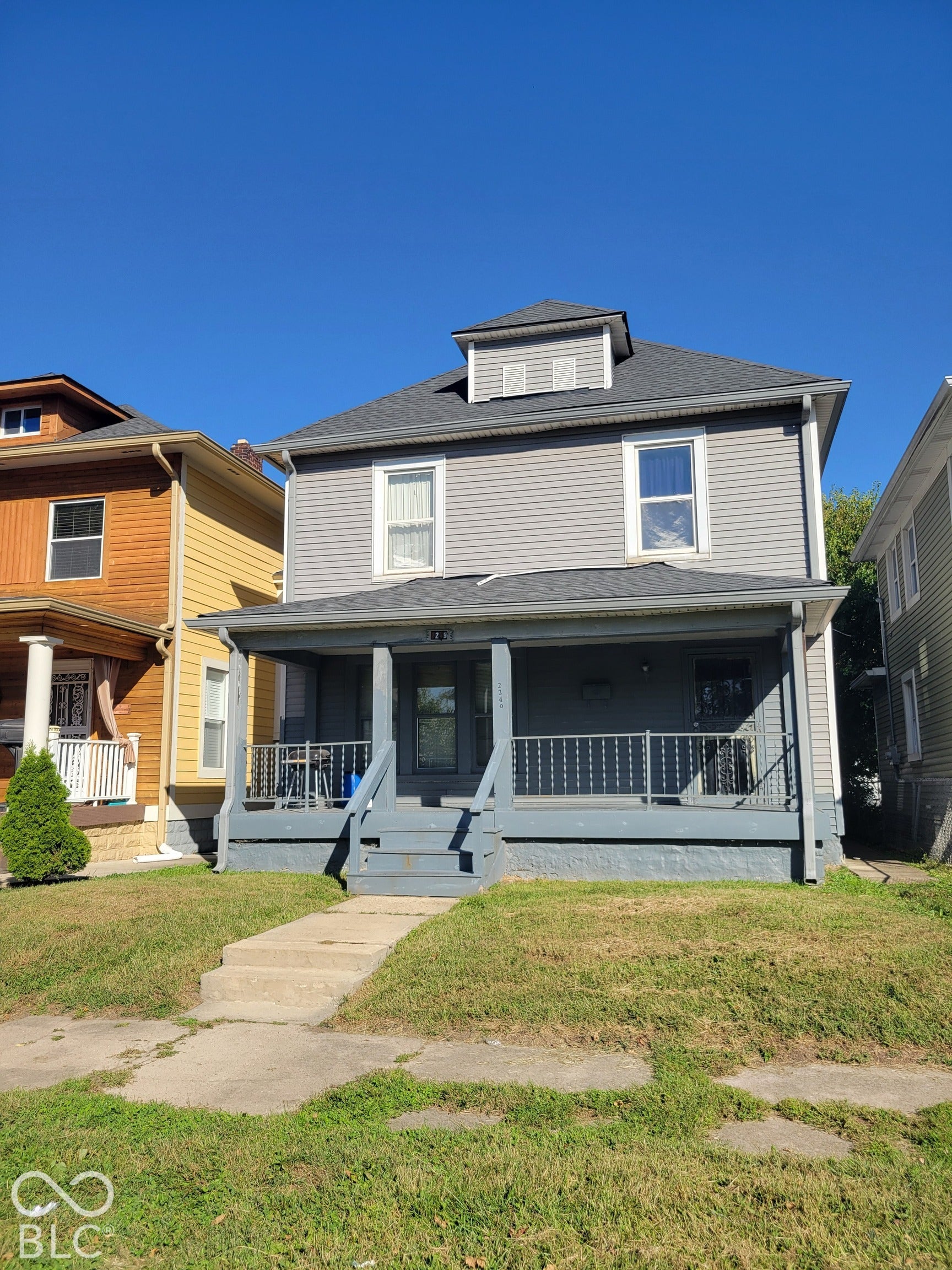 Two-story residence with gray siding, dormer window, and a covered front porch featuring railings