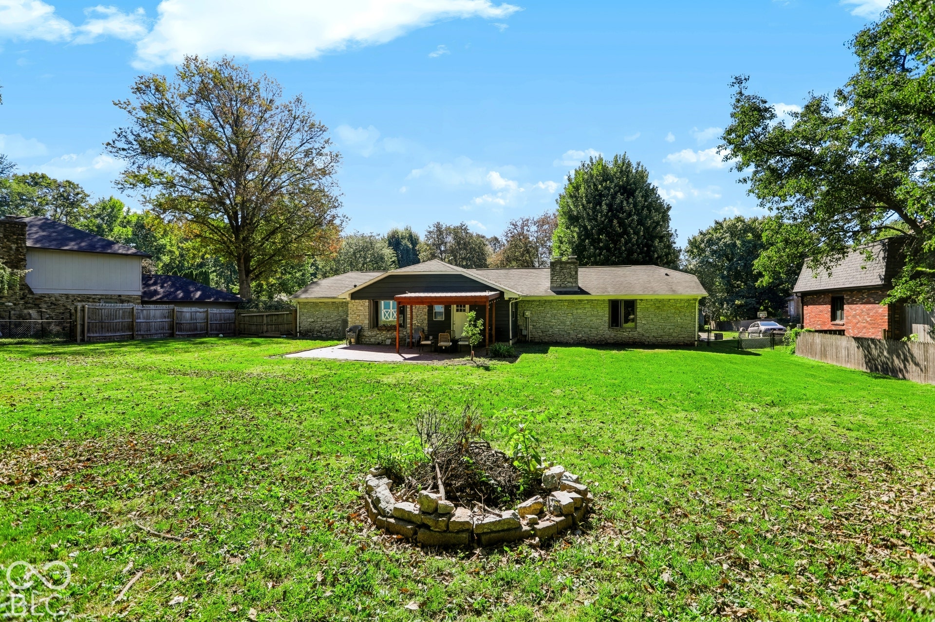 Expansive green lawn with a covered patio, paved outdoor area, and a stone-lined fire pit