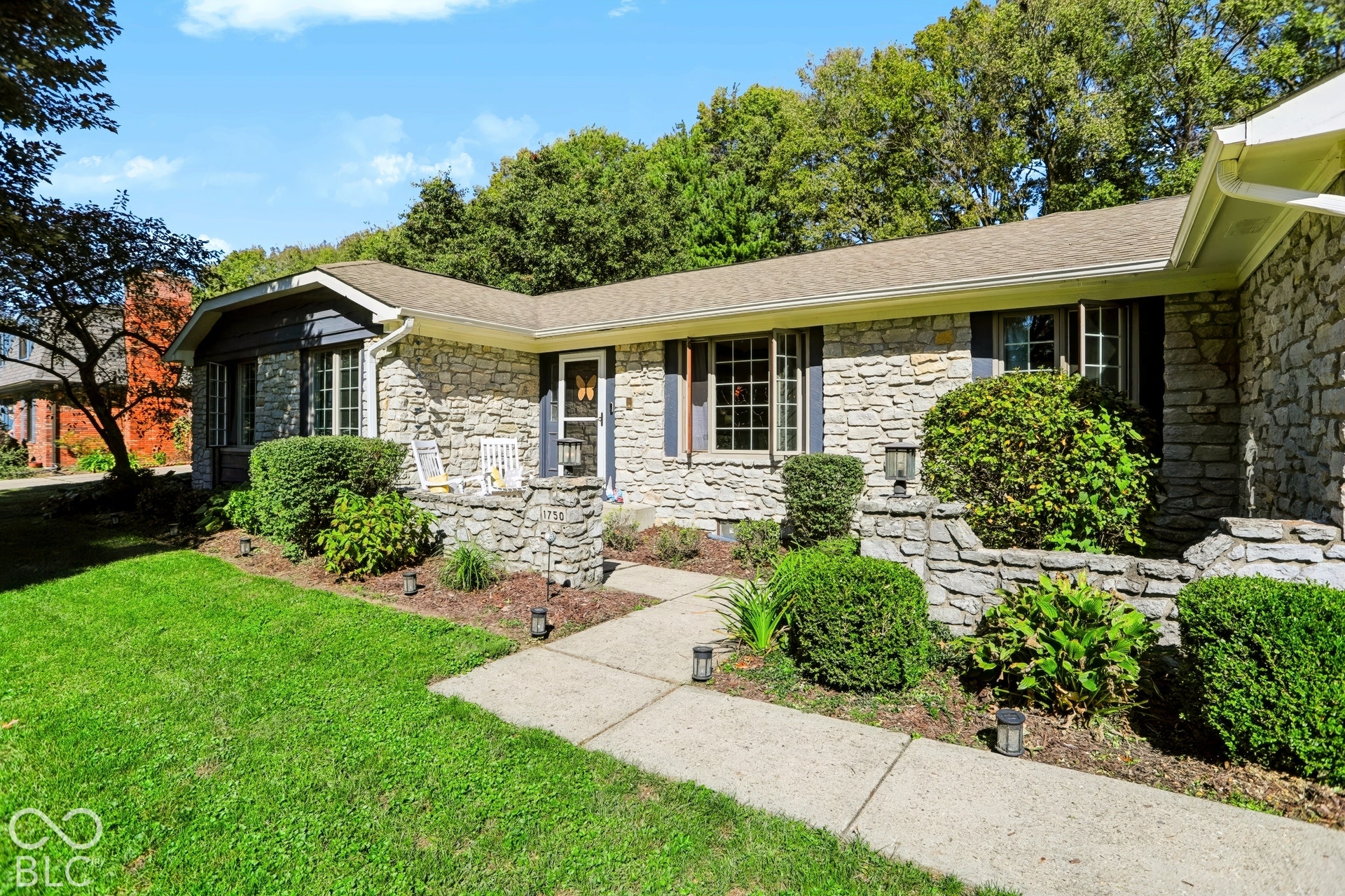 Stone veneer exterior with dark shutters, gabled roofline, and landscaped front yard