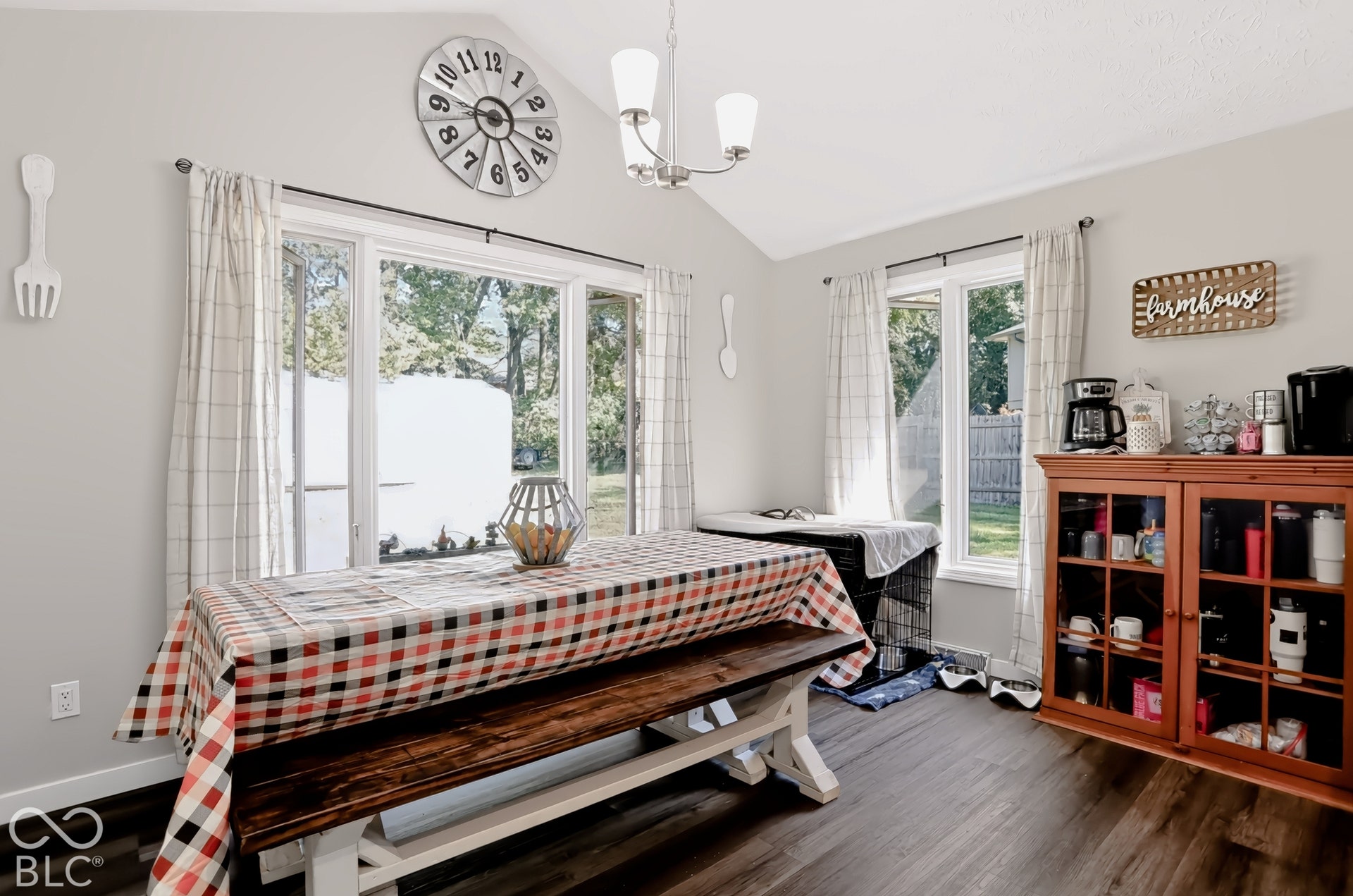 Vaulted ceiling, wood-finish flooring, multiple windows, built-in cabinetry with glass doors, and a chandelier