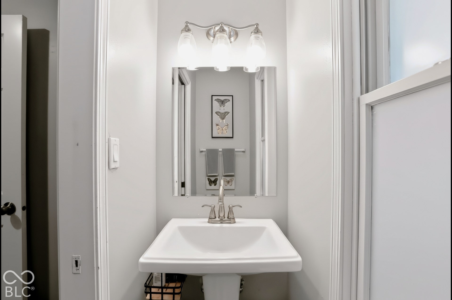 Pedestal sink with a brushed nickel faucet, mirror, and a three-light vanity fixture