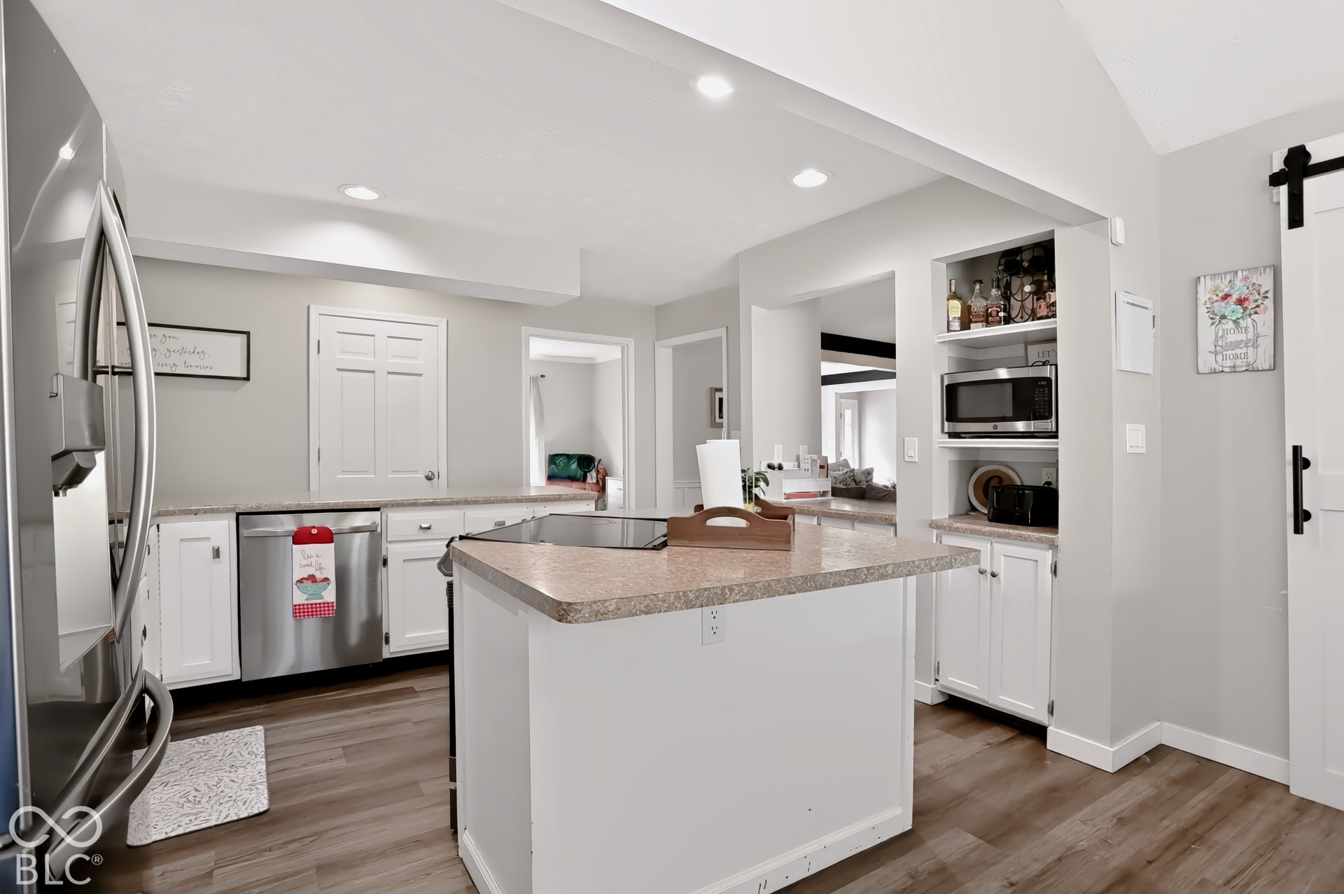 Kitchen featuring an island with a countertop, stainless steel refrigerator, stainless steel dishwasher, built-in shelving, and wood-finish flooring
