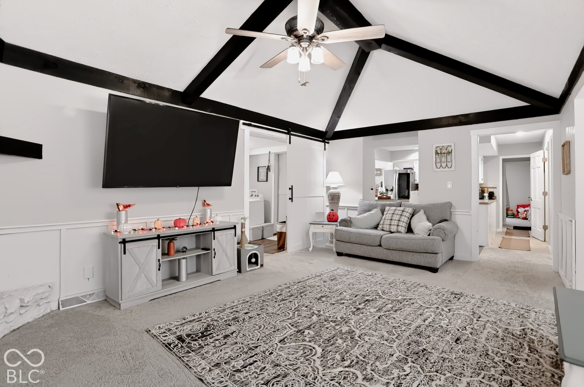 Vaulted ceiling with exposed beams, ceiling fan, white paneled wall trim, carpeted flooring, and a barn door entry