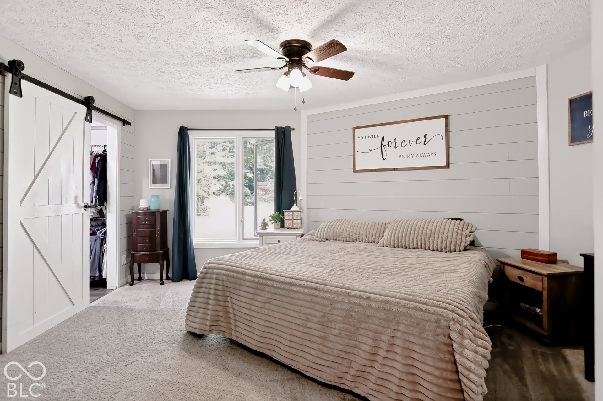 Ceiling fan with integrated lighting, window with white trim, gray shiplap accent wall, white barn door on a black track, and carpeted flooring