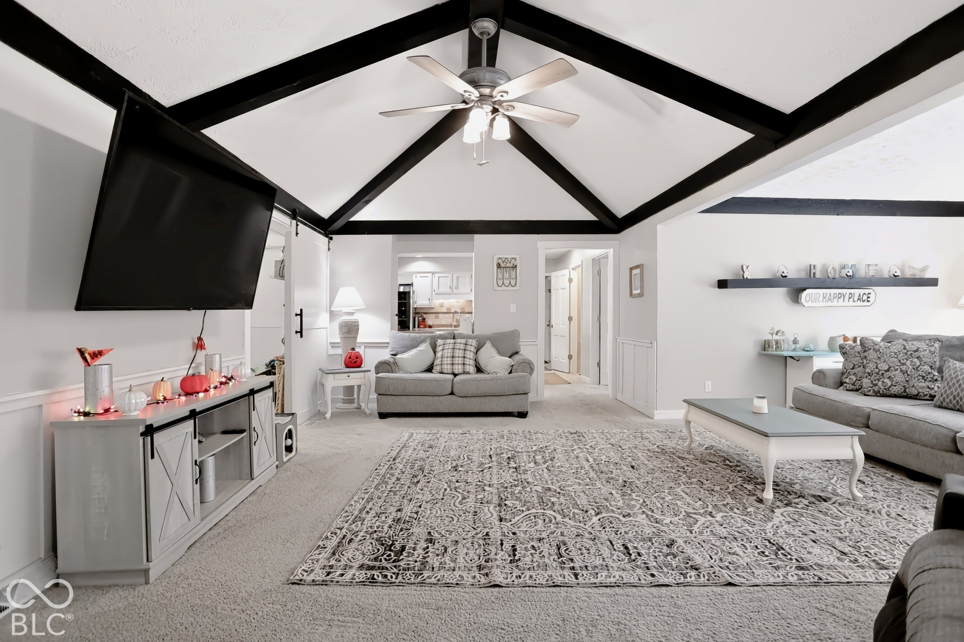 Vaulted ceiling with exposed black beams, ceiling fan, and carpeted flooring