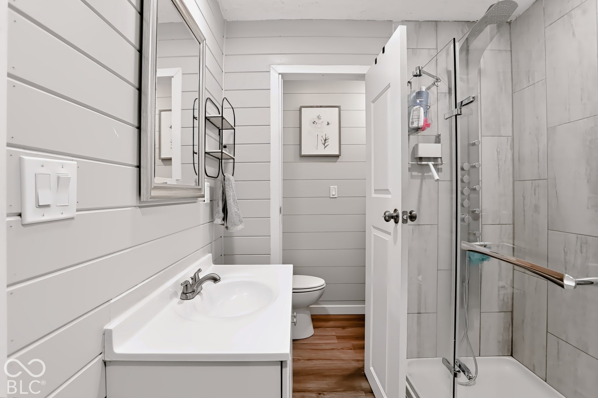 Shiplap wall paneling, vanity with integrated sink, glass-enclosed shower, tiled shower surround, and wood-finish flooring