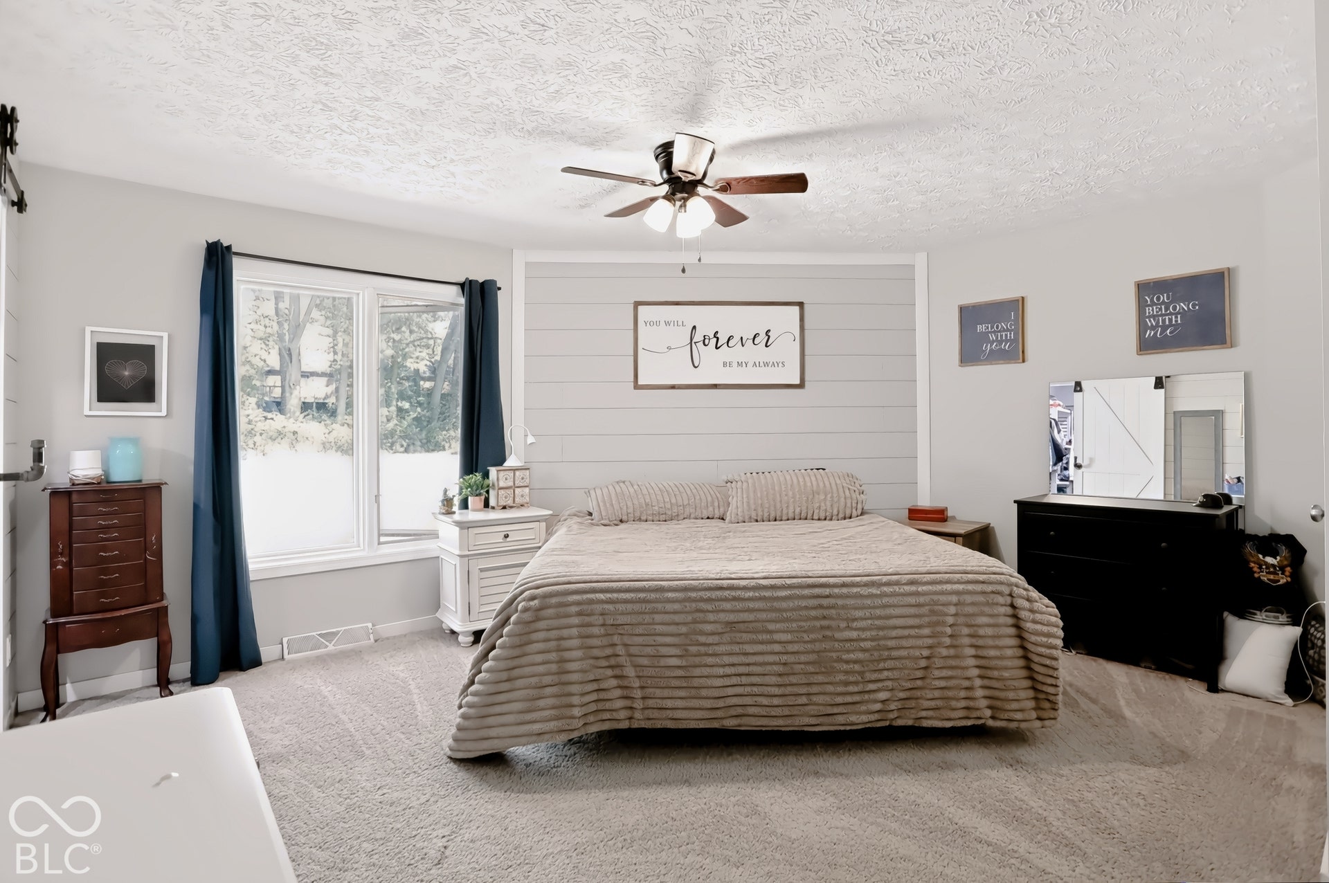 Bay window offering natural illumination, light gray shiplap accent wall, ceiling fan with integrated lighting, wall-to-wall carpeting, and light gray painted walls