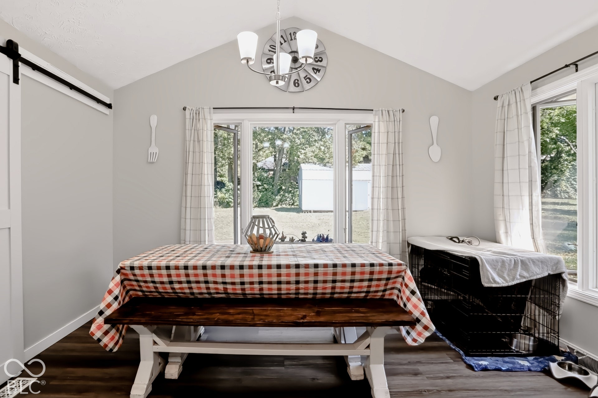 Vaulted ceiling, wood-finish flooring, white trim, track barn door, and a multi-light chandelier