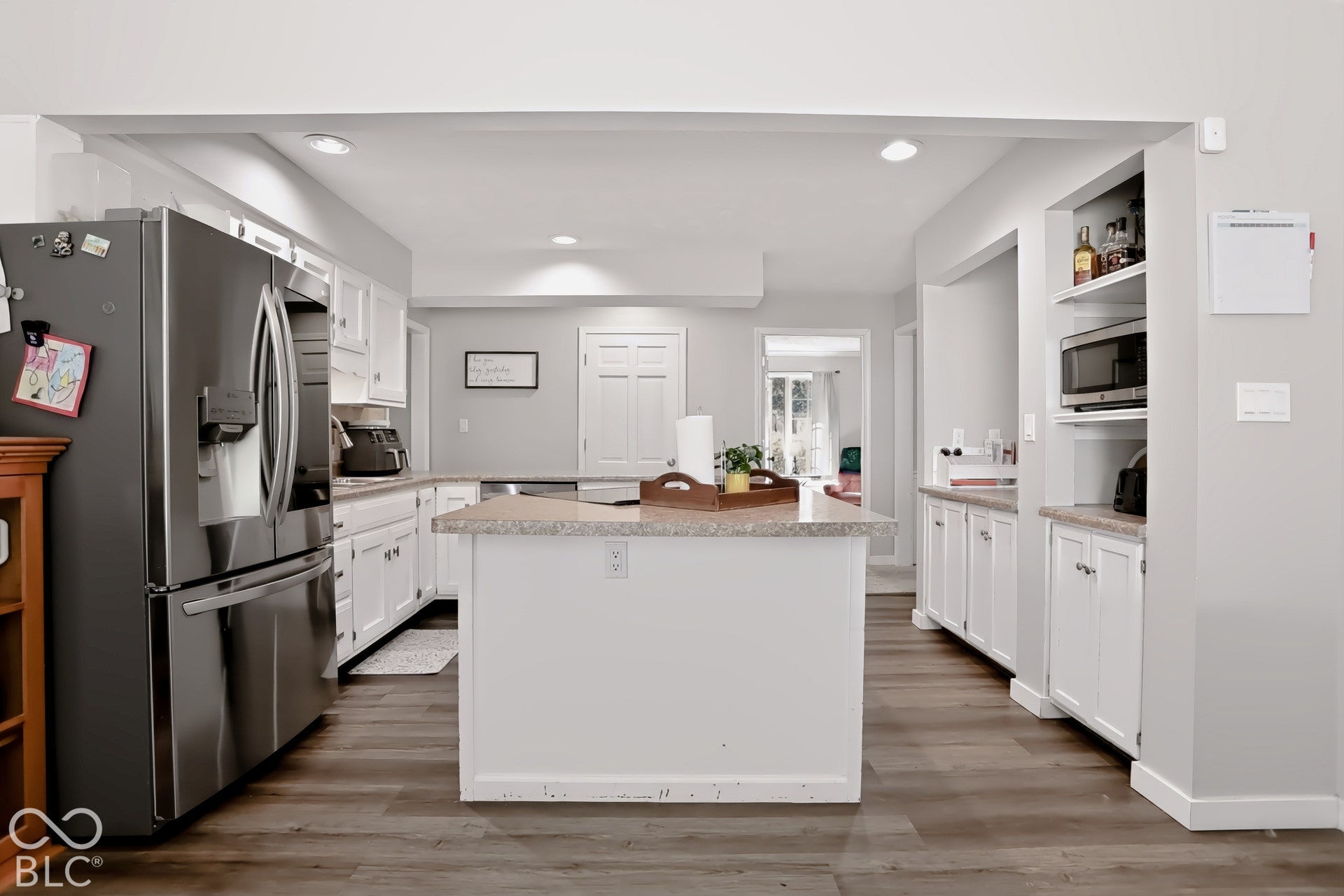 Kitchen featuring wood-finish flooring, white cabinetry, a central island with a light-toned countertop, recessed lighting, and stainless steel appliances