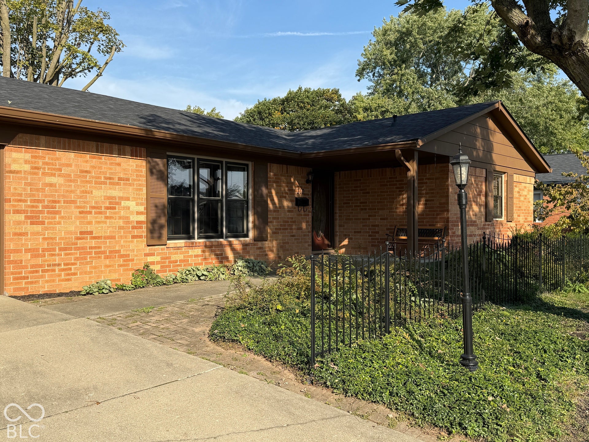 Brick exterior with dark shutters, covered front entry, paved walkway, and a black wrought iron fence